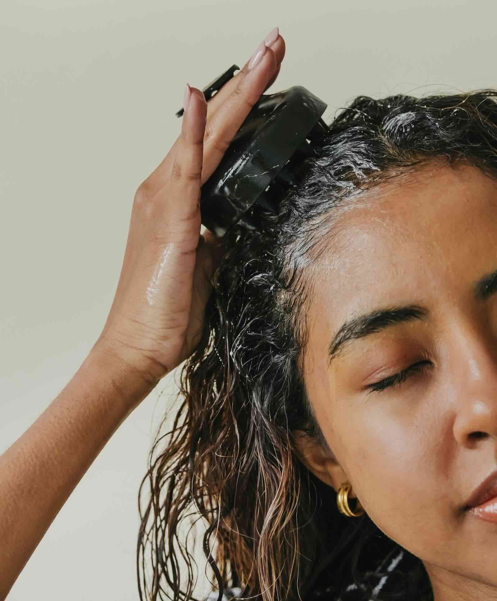 Close-up of a woman applying scalp treatment to naturally curly hair, emphasizing healthy roots, moisture, and intentional hair care.