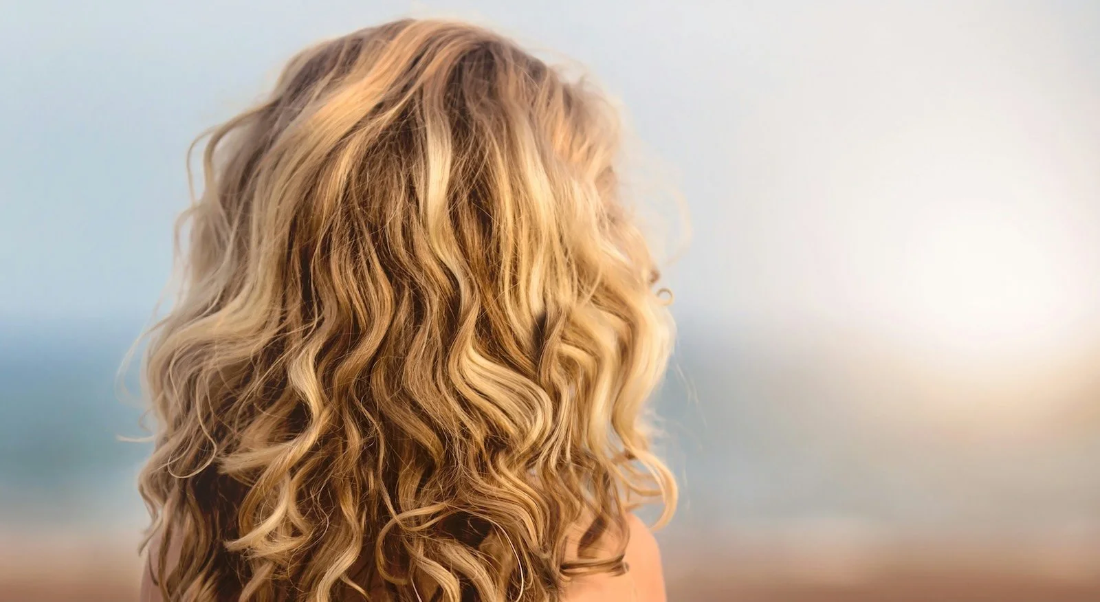 Warm blonde balayage with natural curl and summer dimension — lived-in color by Albert Narcisse, Master Hair Colorist NYC
