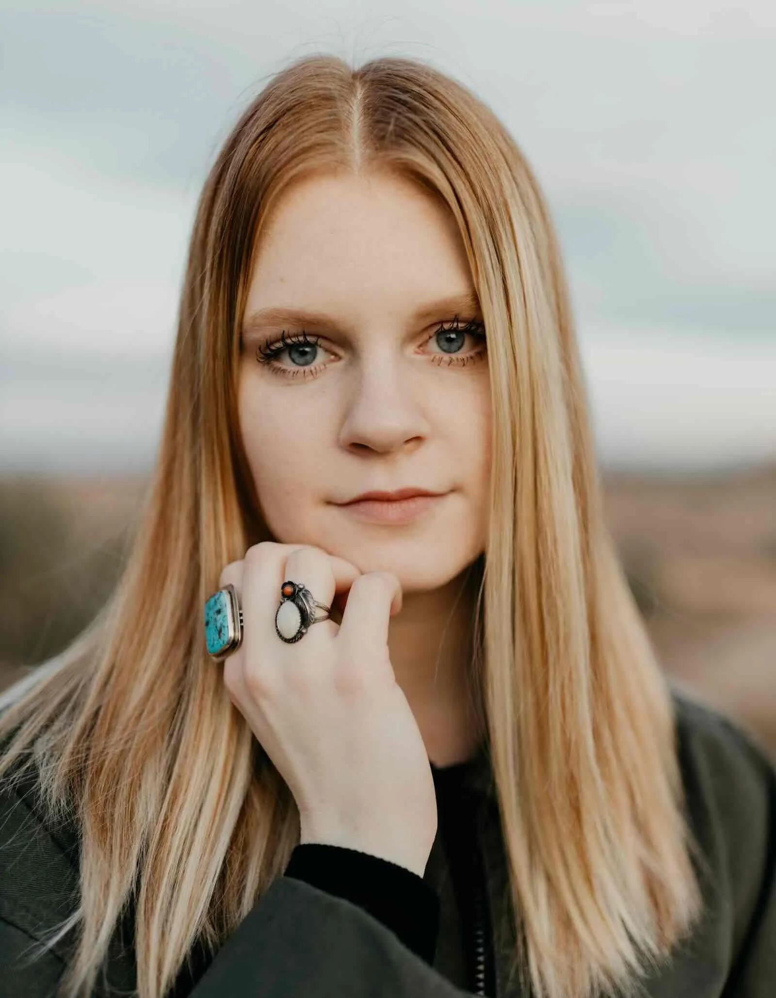 Young woman with warm blonde highlights and natural strawberry-blonde base, long straight hair, turquoise and coral rings, thoughtful expression — Hair & Life AlbertColor NYC