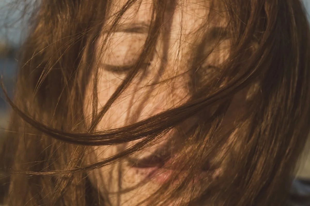 Long auburn hair blown across a woman's face in warm late-summer sunlight