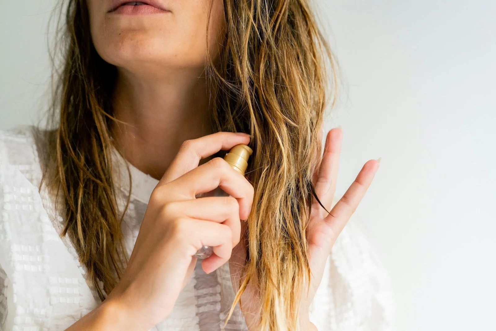 Woman applying hair mist spray through damp balayage ends for summer hair care