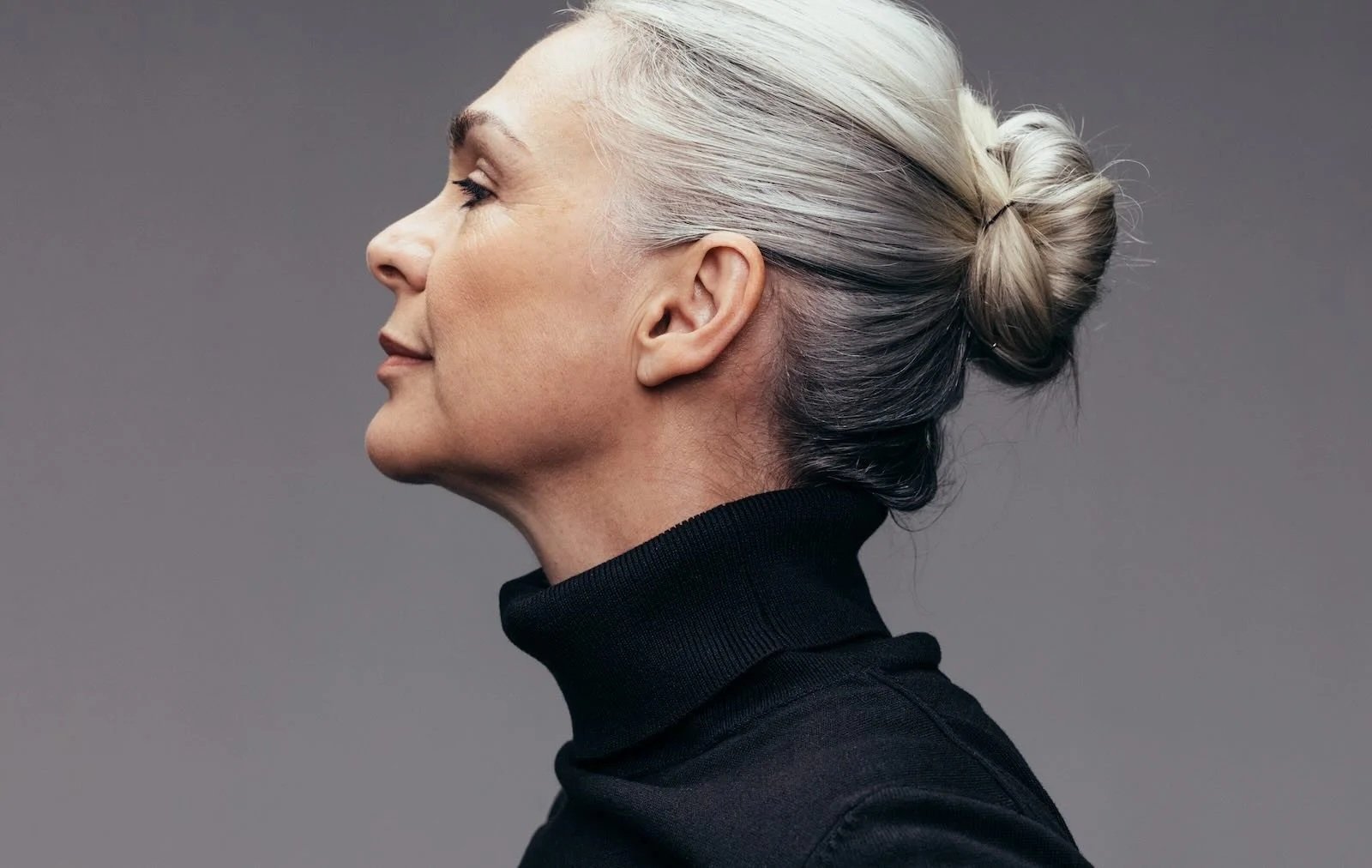 Elegant woman with naturally gray hair styled in a low bun, shown in profile