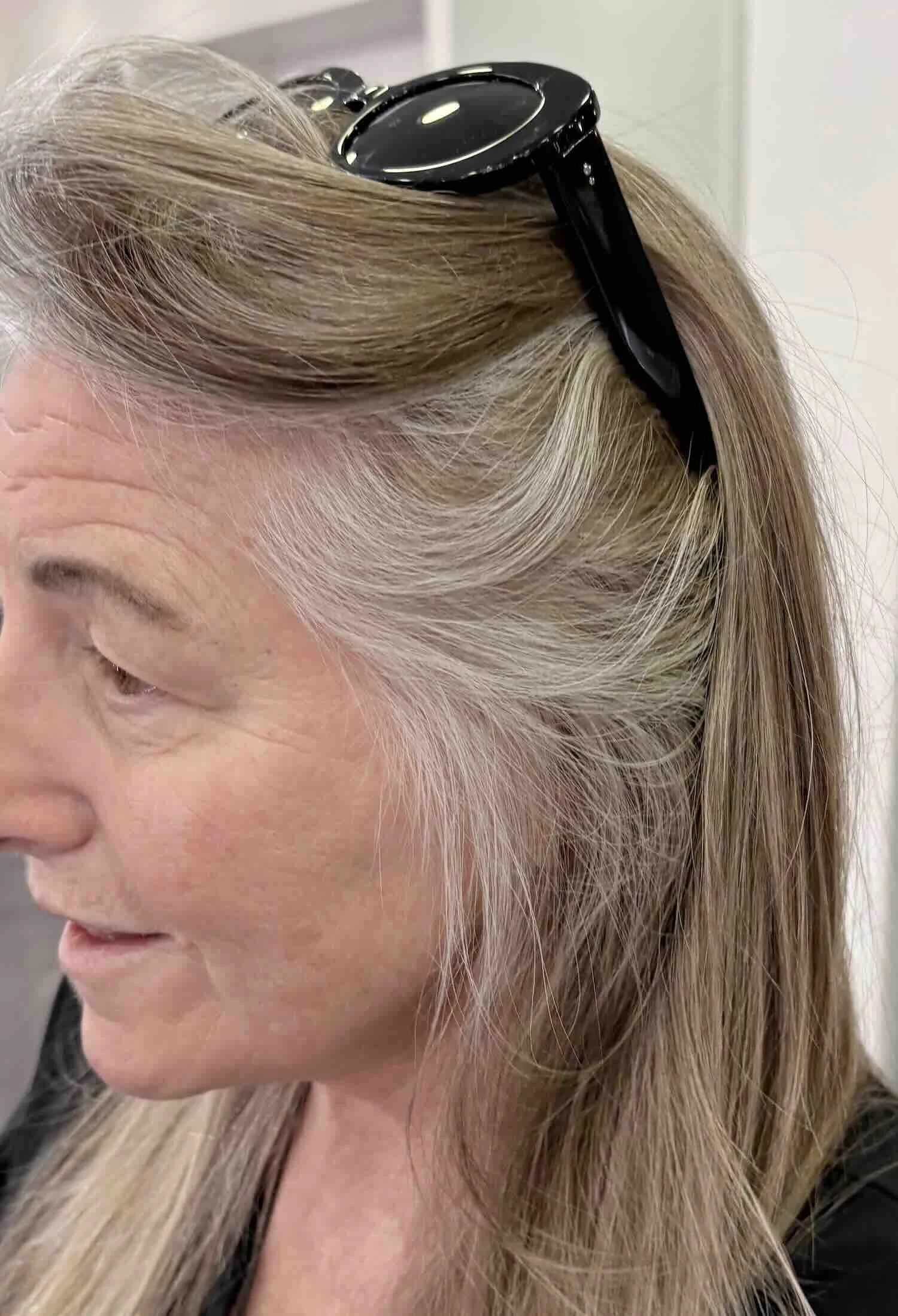 Woman showing natural gray hair pattern at temples and crown, ash-blonde through the length, pulled back casually — AlbertColor NYC