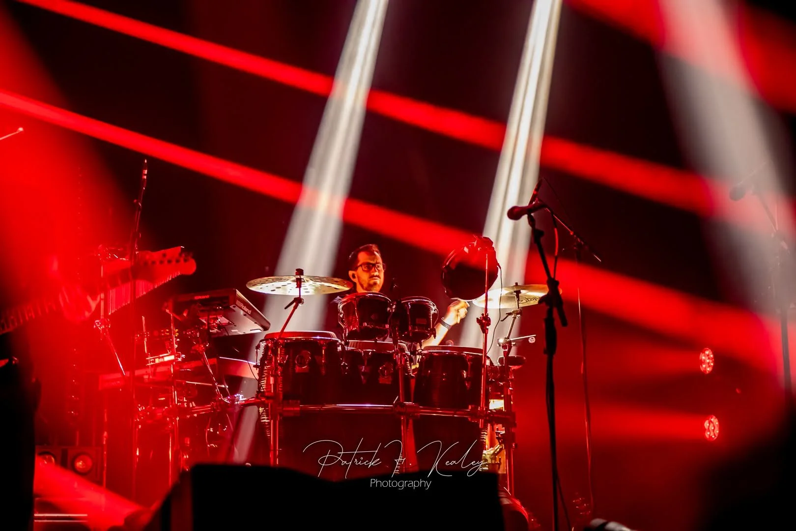 Musician playing drums on stage illuminated by red and white stage lights.