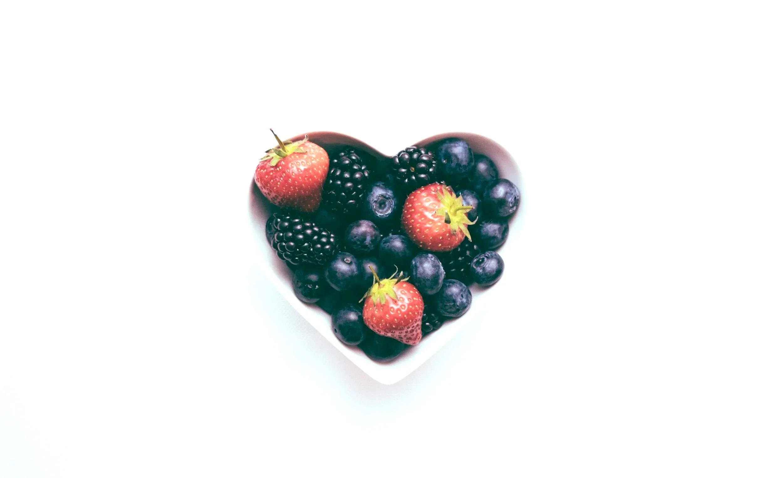 A heart-shaped dish filled with strawberries, blackberries, and blueberries on a white background.