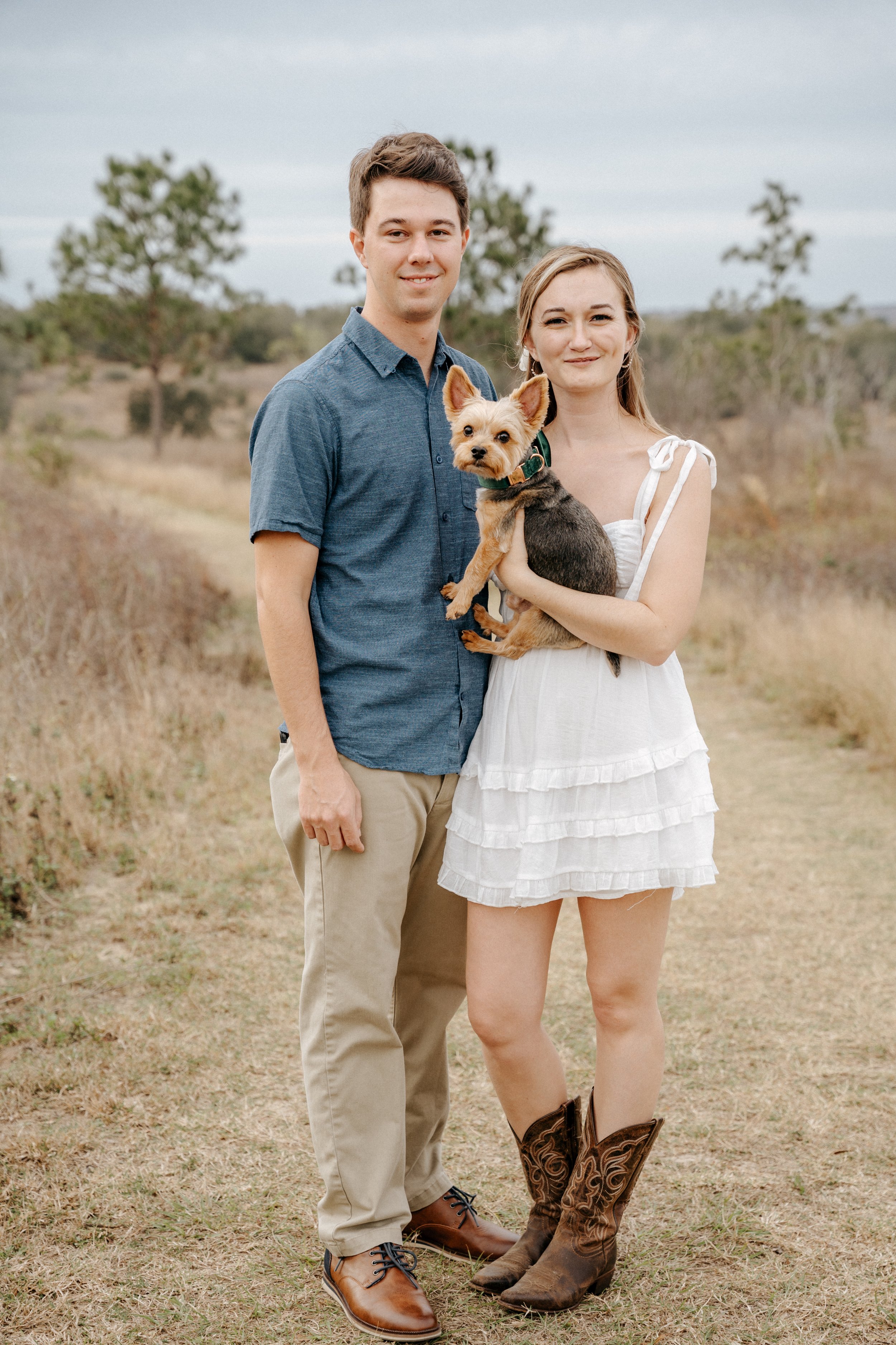 A photo of the owners of The Mini Farmhouse Co, depicting a young couple with a dog standing outdoors on a grassy path with trees in the background.