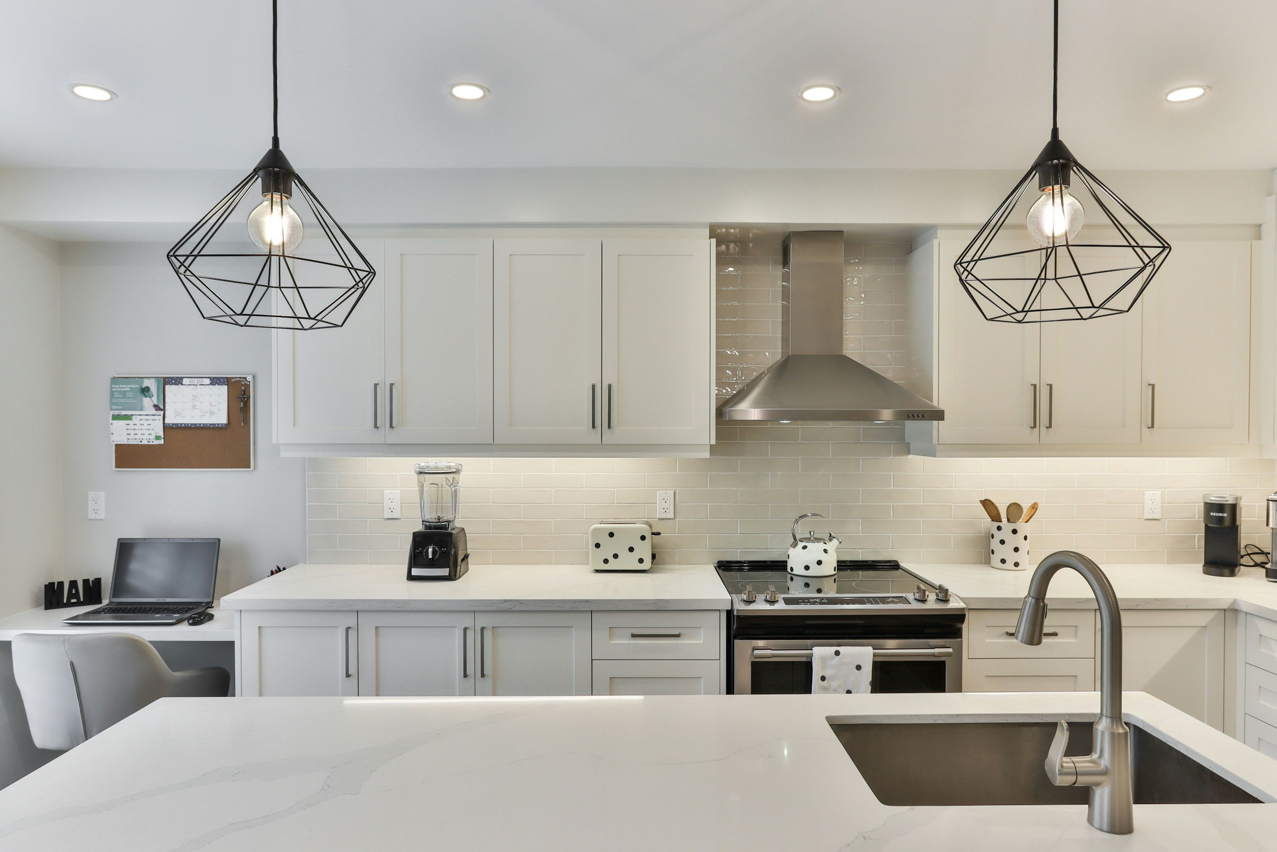 Modern kitchen with white cabinets, brick backsplash, stainless steel range hood, black and white patterned accessories, pendant lights, and a kitchen island.