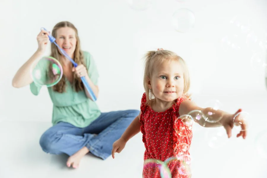 Happy young woman and baby girl smiling and playing together with a white ball in a bright room.