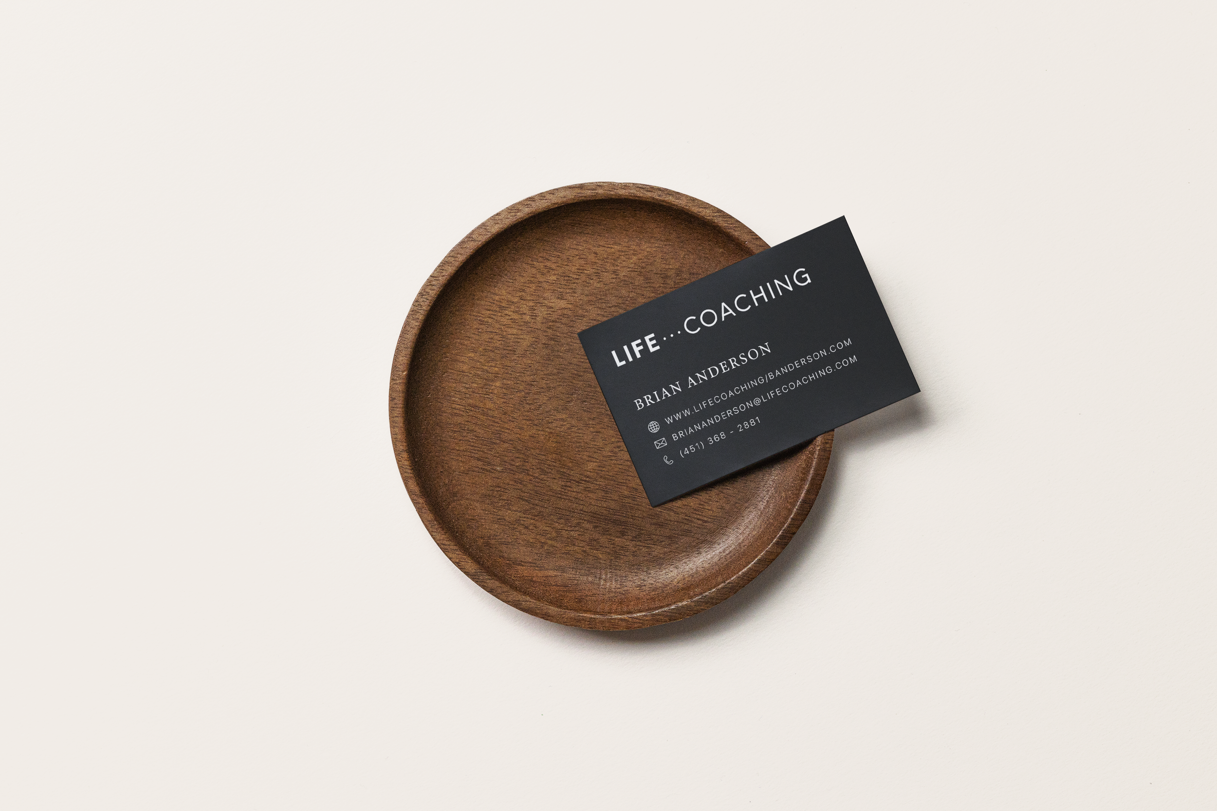 A business card for Life Coaching placed on an empty round wooden dish against a plain white background.