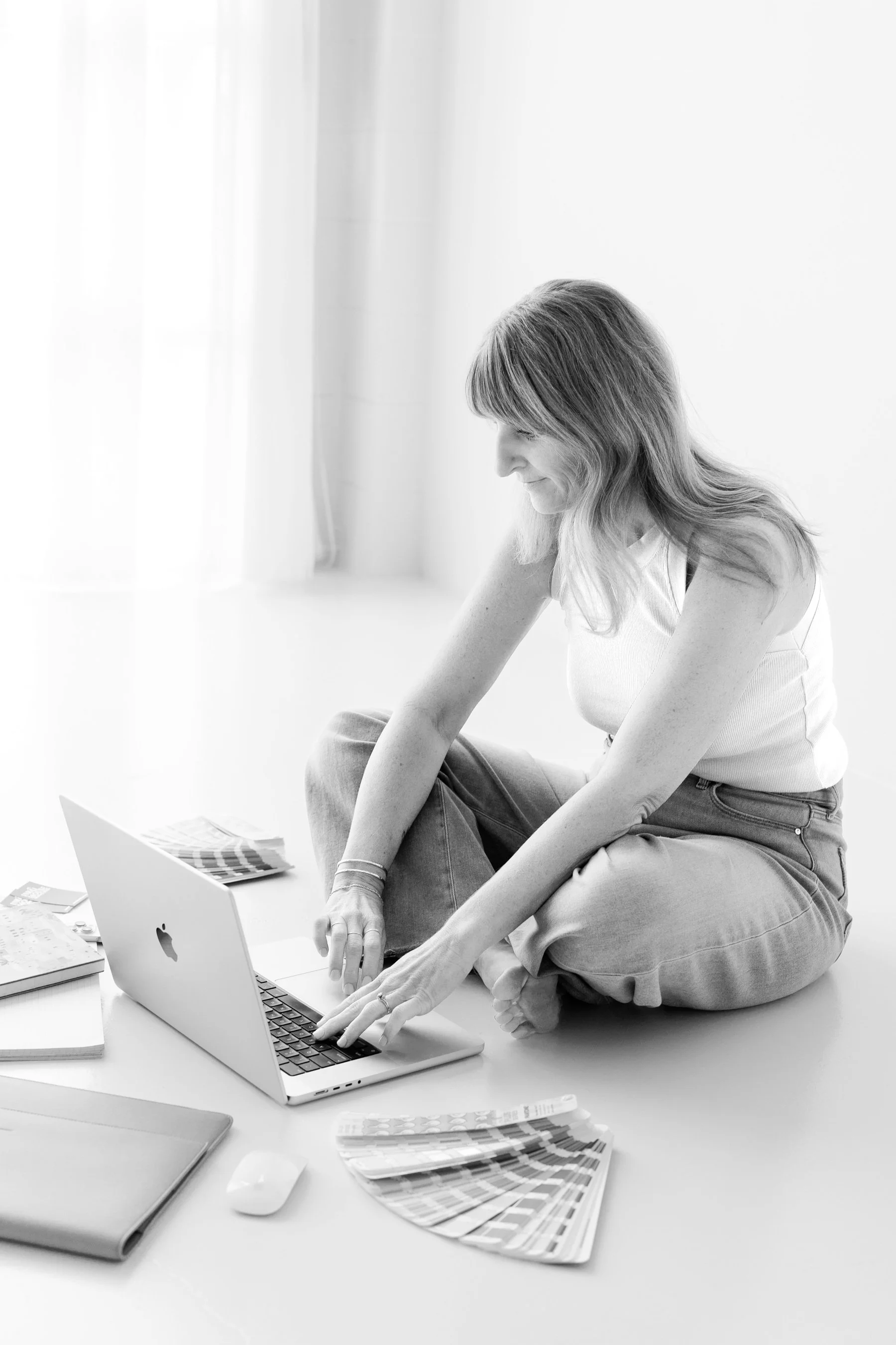 Woman with laptop, color palettes, mouse, and design books on floor