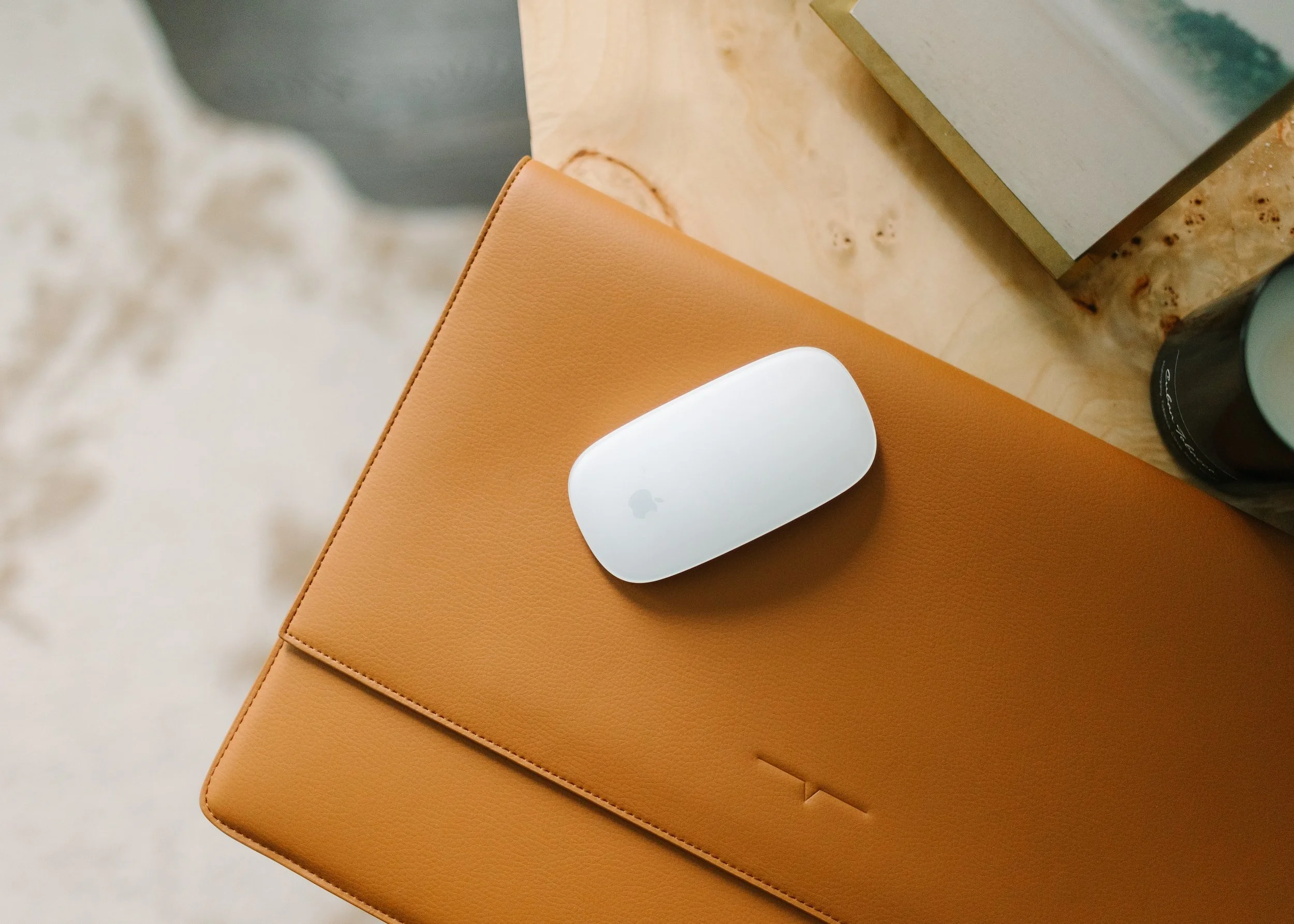 An Apple AirPods case on top of a tan leather notebook placed on a wooden surface