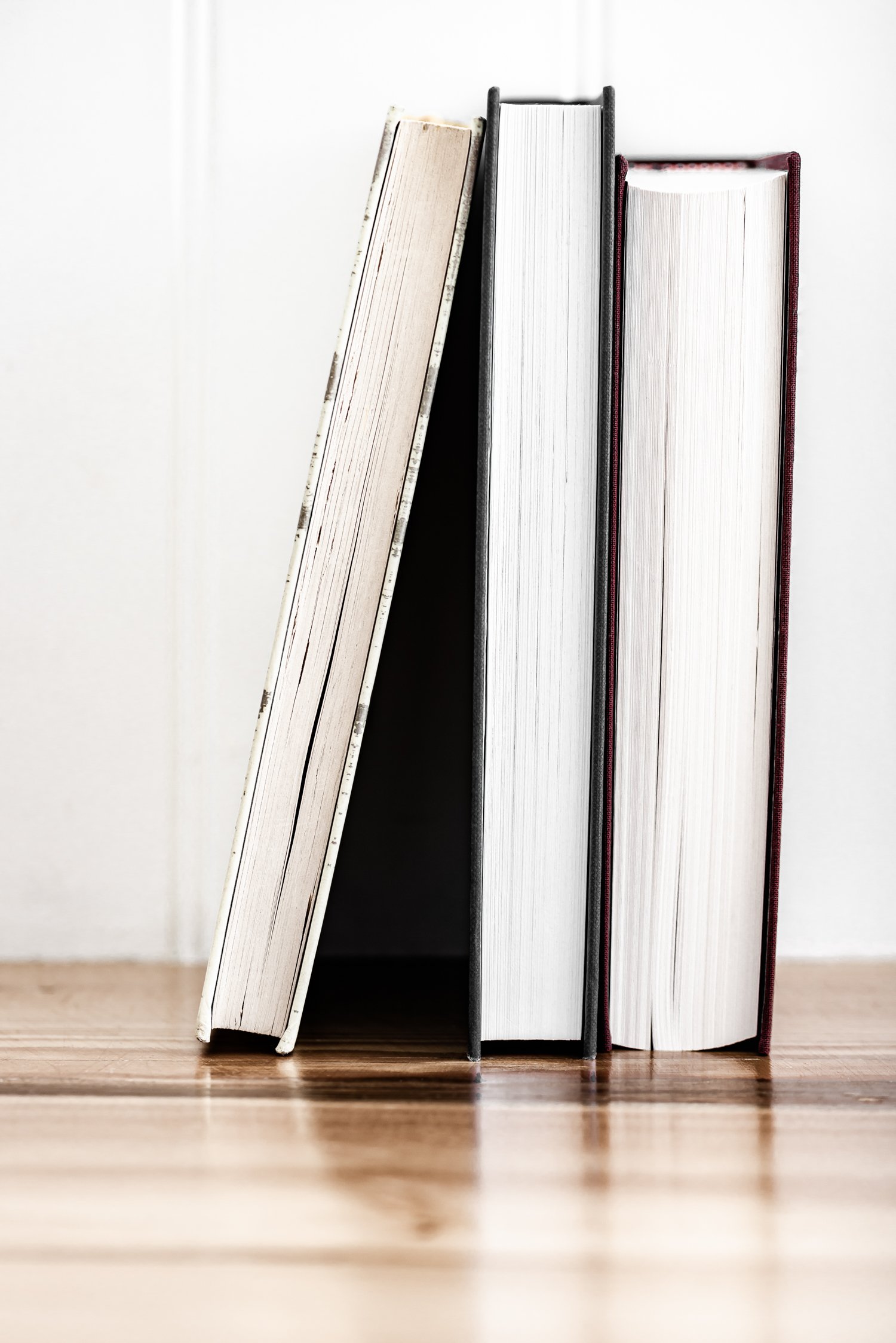 Four books standing upright on a wooden surface, with a white wall in the background.