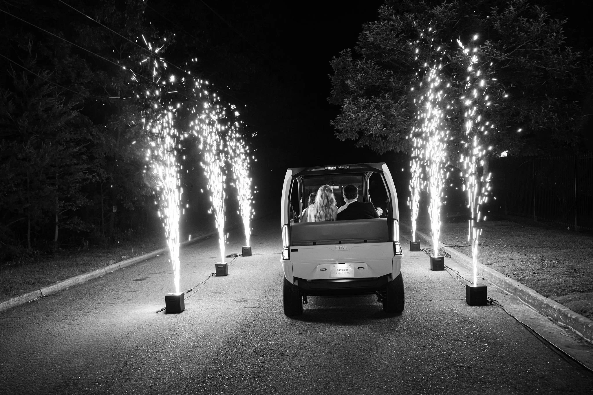 A golf cart driving down a street at night with fireworks on either side and in the background, celebrating an event.