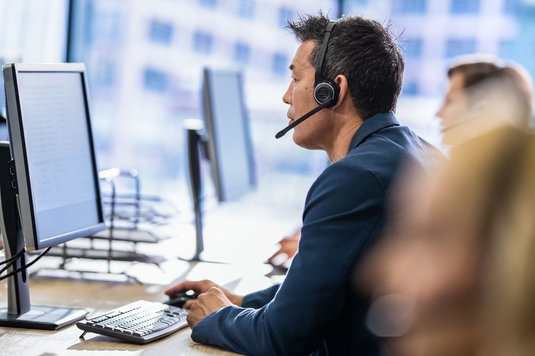 Man wearing a headset working at a computer in an office.