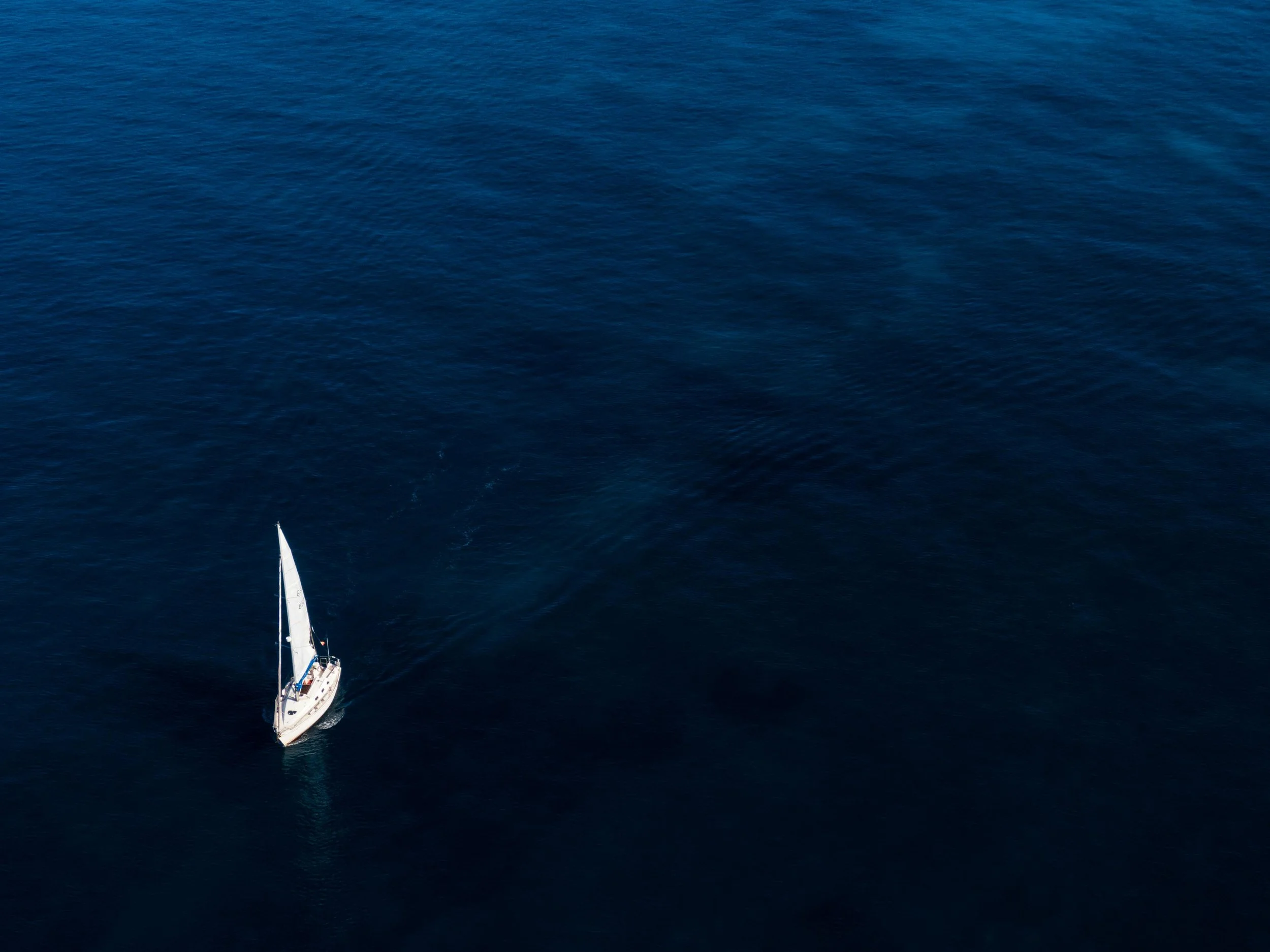 A sailboat with white sails on deep blue ocean water