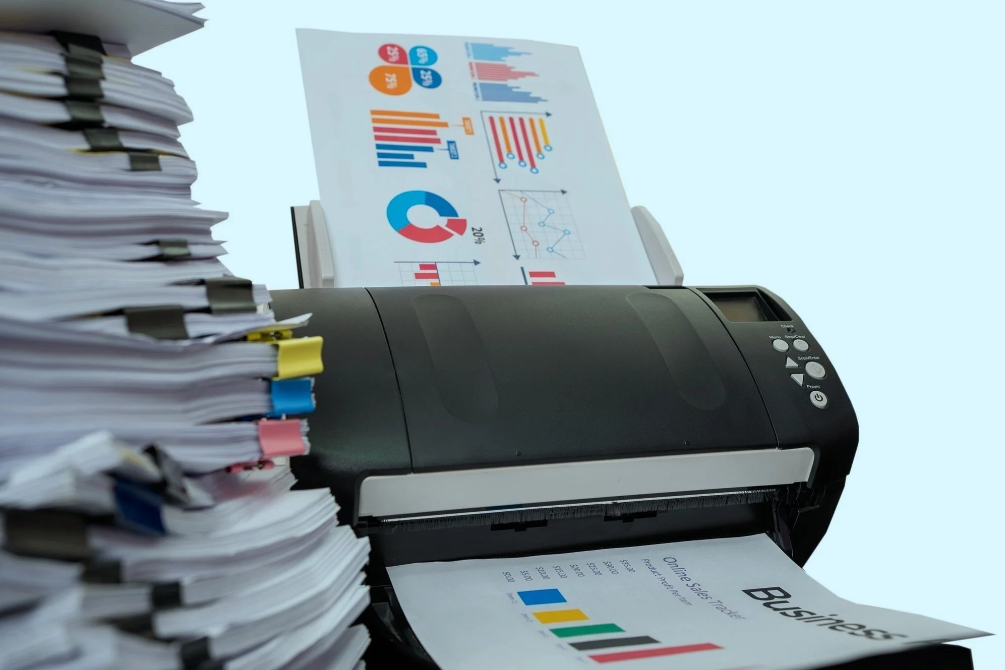 A copier machine printing a document titled 'Business' with colorful bar graphs and charts, surrounded by a large stack of paper on the left side.