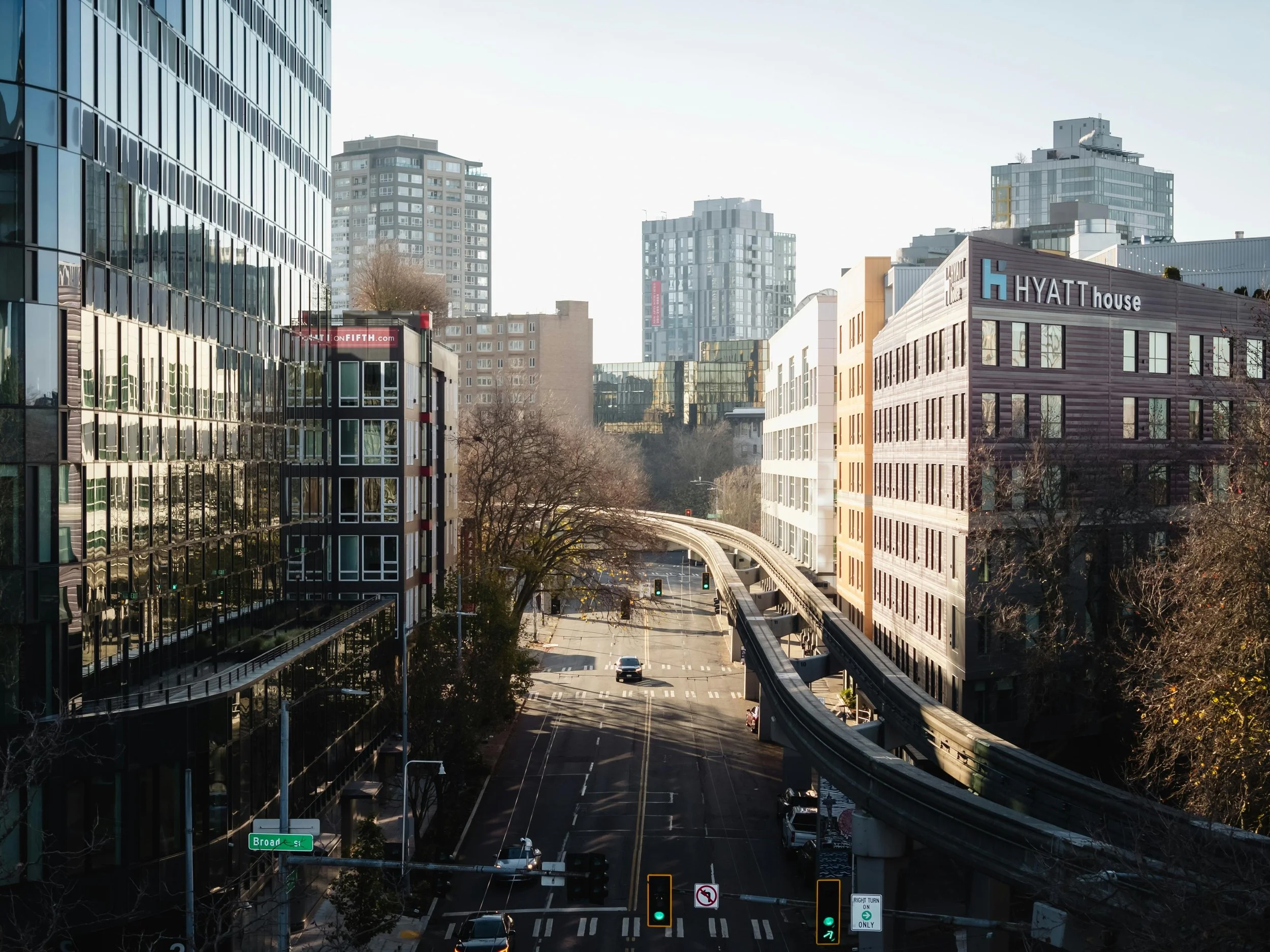 City scene with tall modern buildings, a street with cars, and an elevated train track, taken during daylight with clear weather.