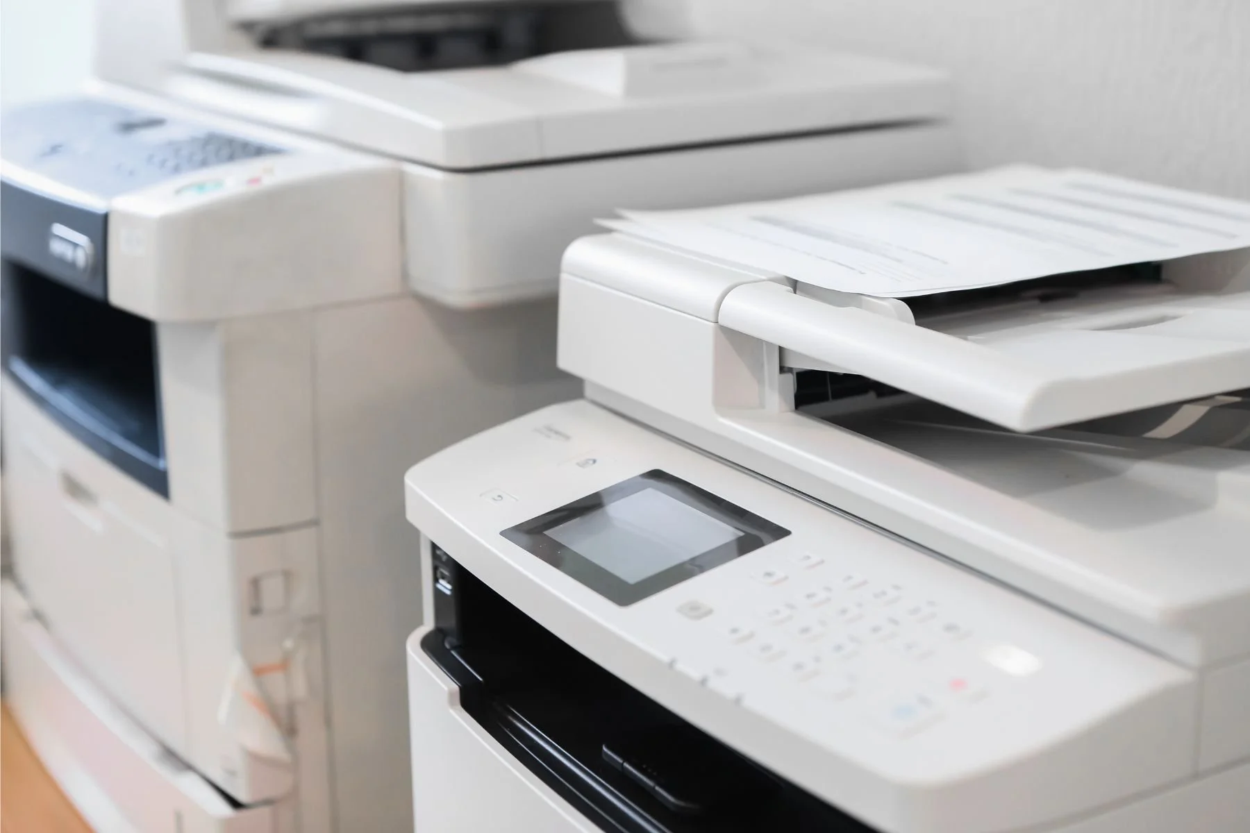 Close-up of two office multifunction printers with paper trays and control panels.
