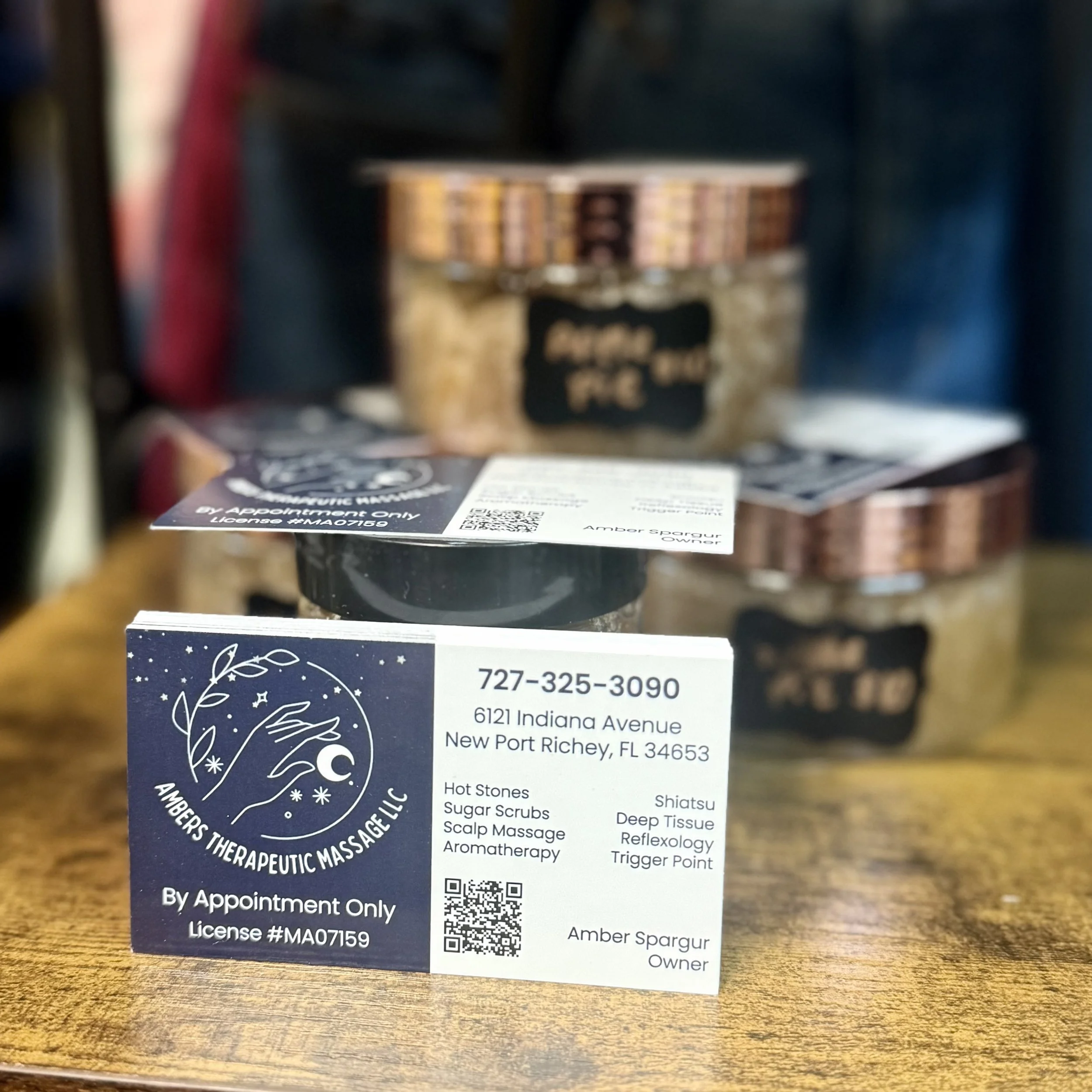 Amber’s Therapeutic Massage business card displayed on a wooden surface in downtown New Port Richey, Florida, featuring massage services, contact information, and owner Amber Spargur.