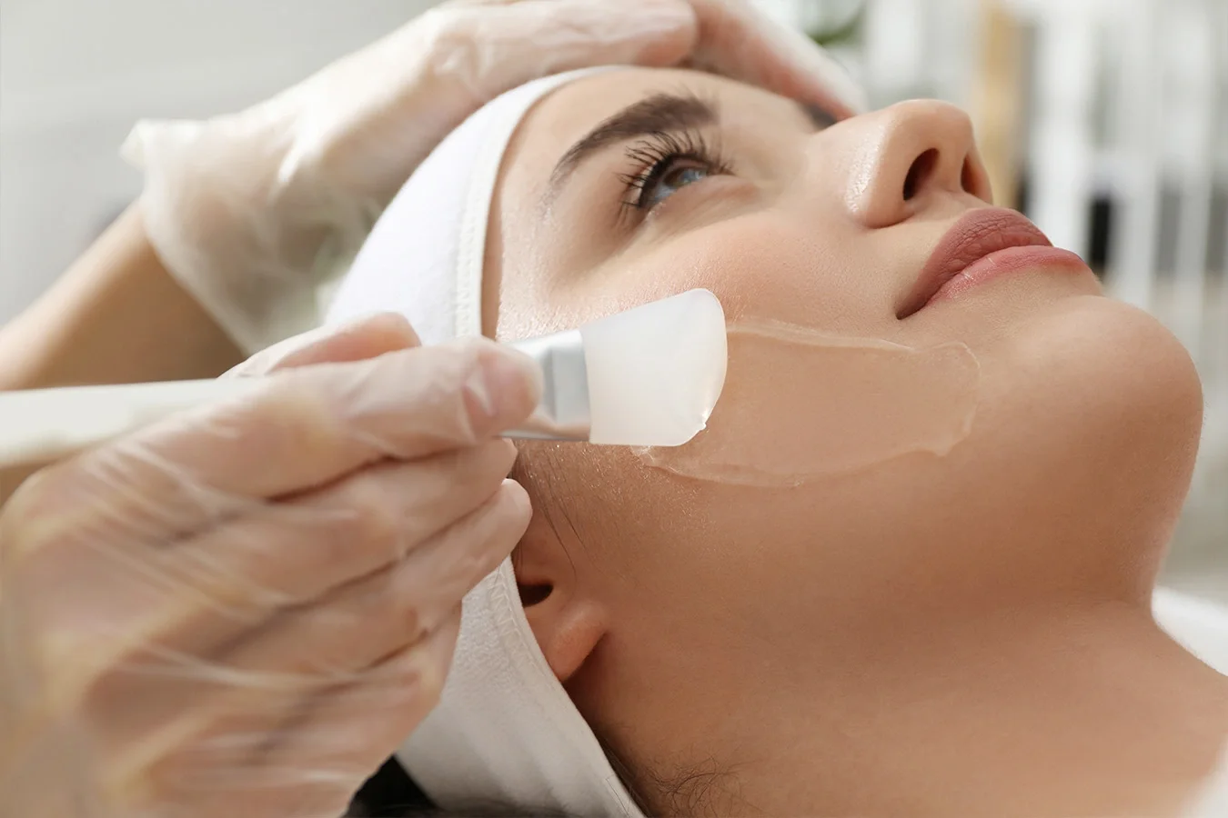 Close-up of esthetician applying a chemical peel solution to a woman’s face during a professional facial treatment session.