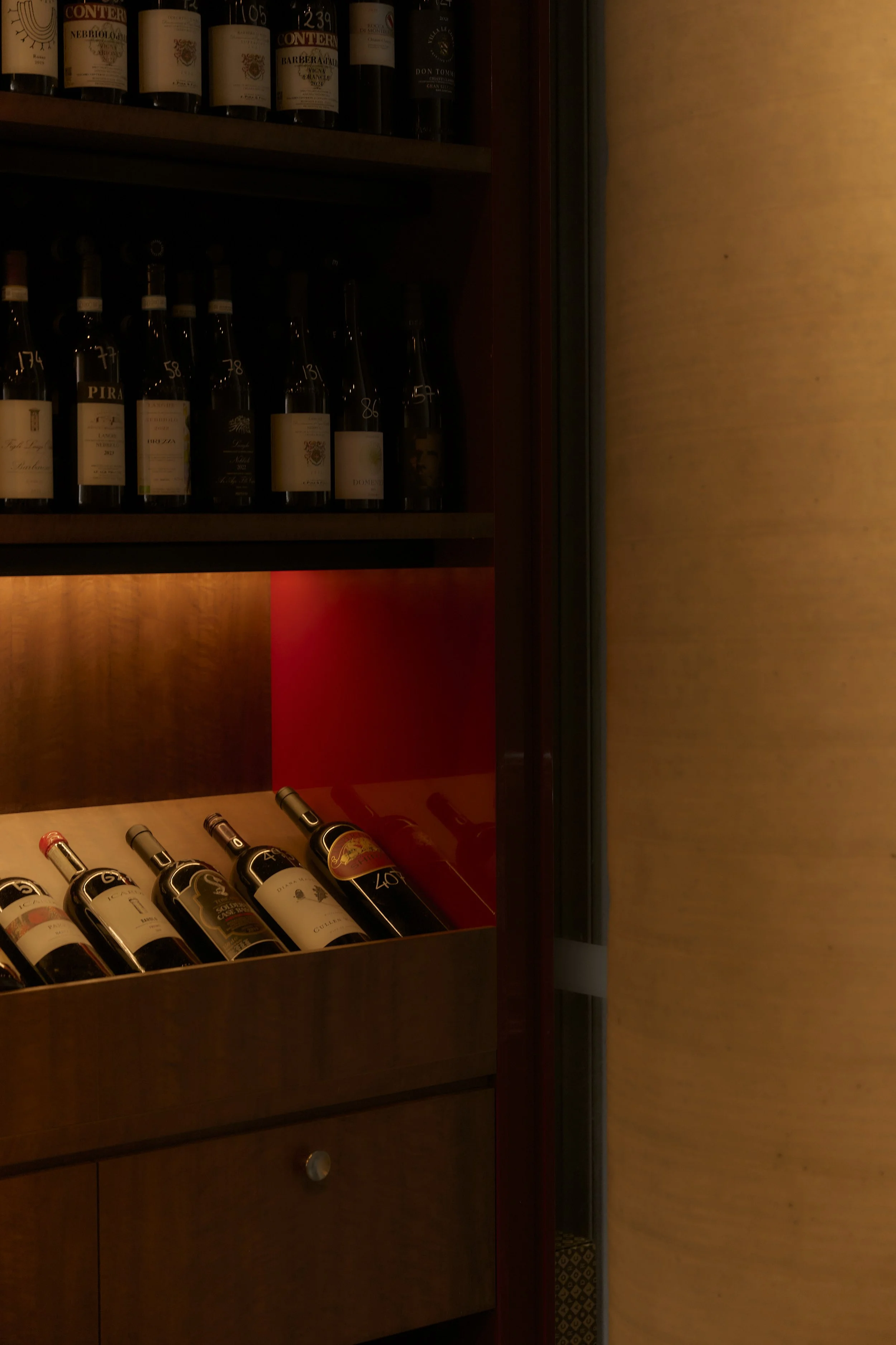 A display of wine bottles in a wooden cabinet with shelves, illuminated by warm lighting.