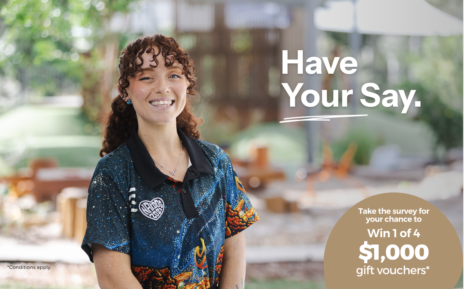 A young woman with curly red hair, smiling and wearing a colorful, space-themed shirt with patches, standing outdoors in a green, sunny backyard. Overlaid text reads 'Have Your Say' with additional smaller text about a survey and a chance to win $1,000 gift vouchers.