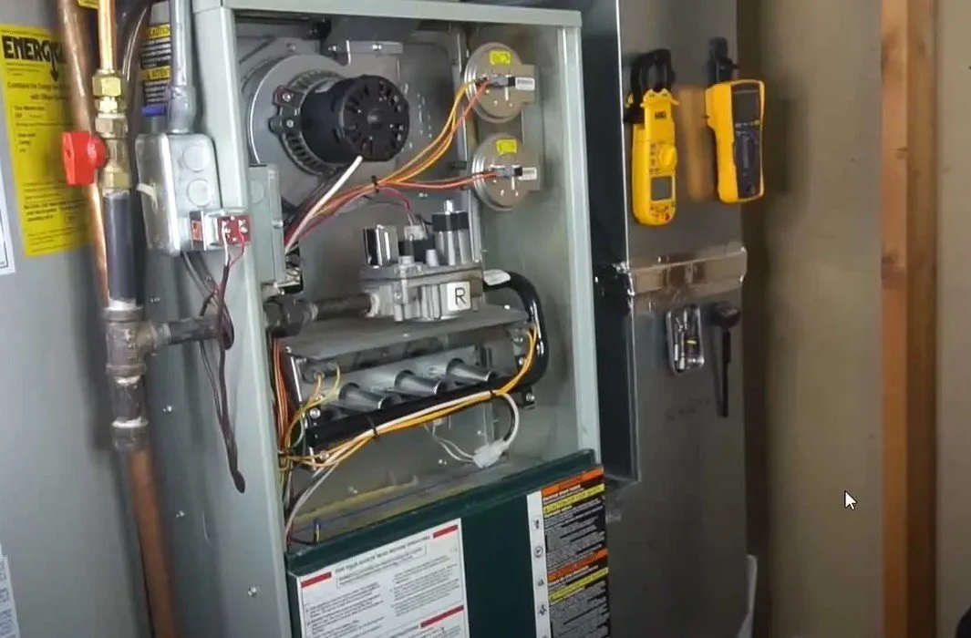 Open furnace or air handler with internal components, tools attached to the side, and a yellow energy guide label.