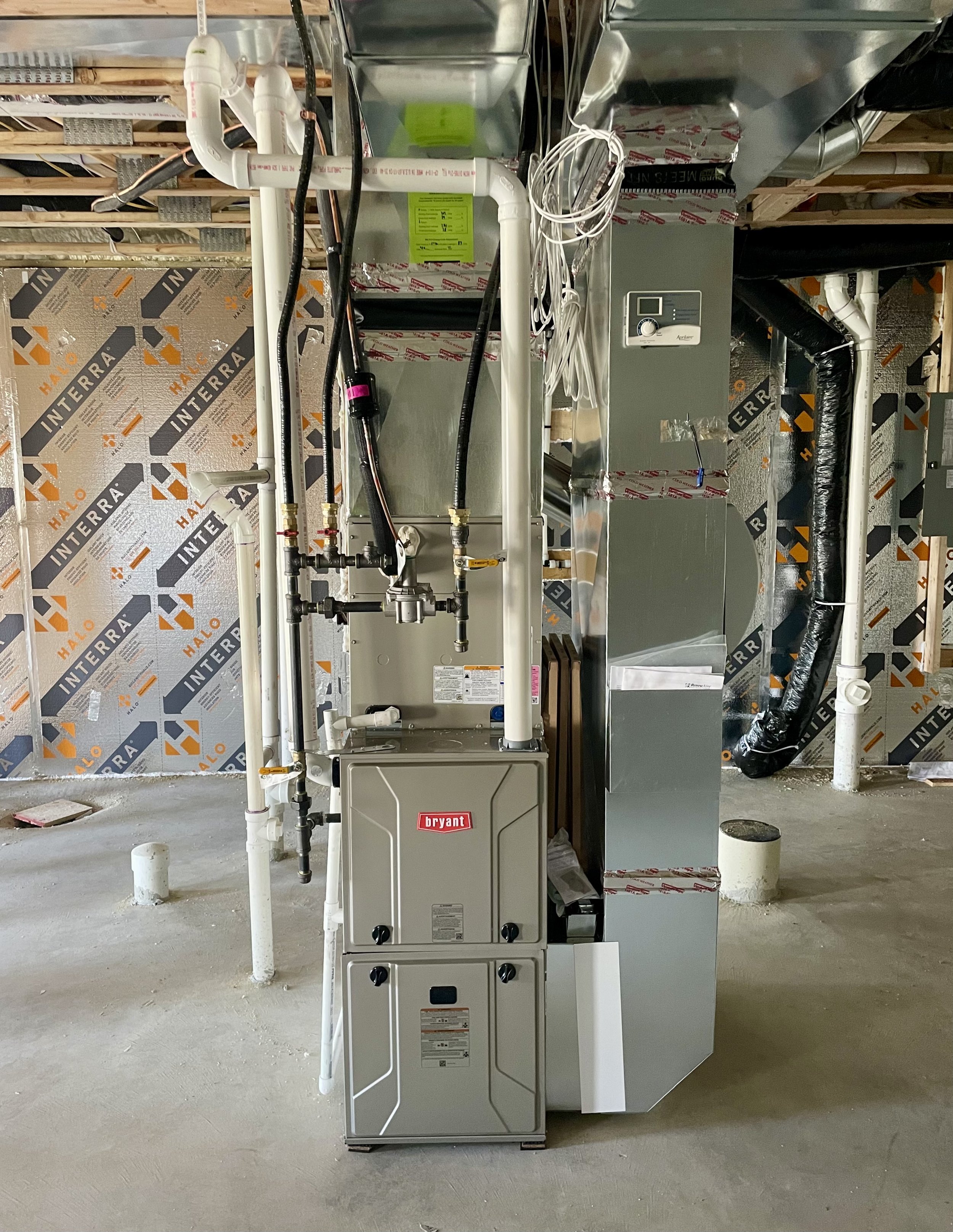 Construction site with unfinished walls and HVAC equipment, including pipes, ducts, and a Bryant furnace.
