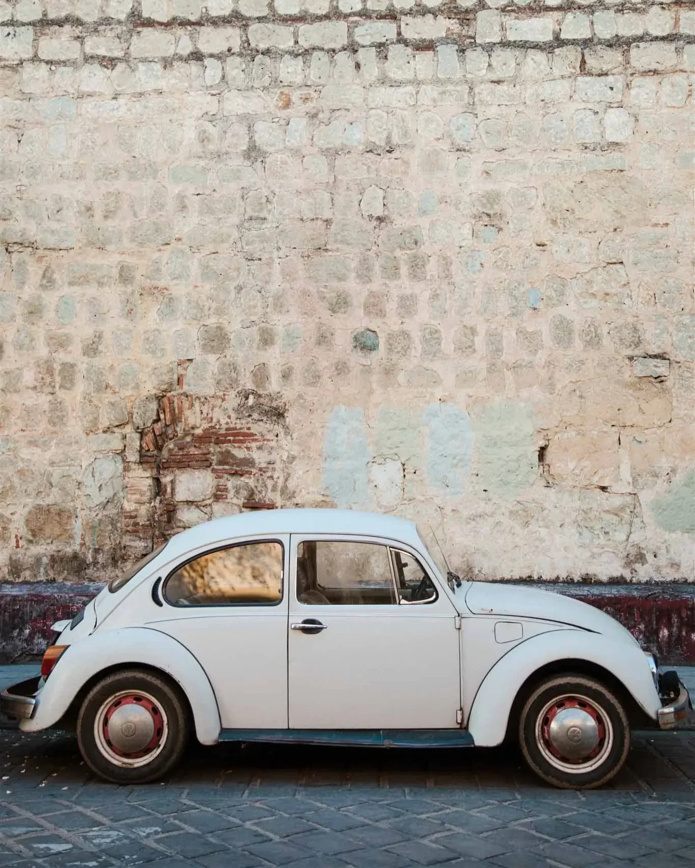 A vintage white Volkswagen Beetle parked in front of an old, weathered brick wall.