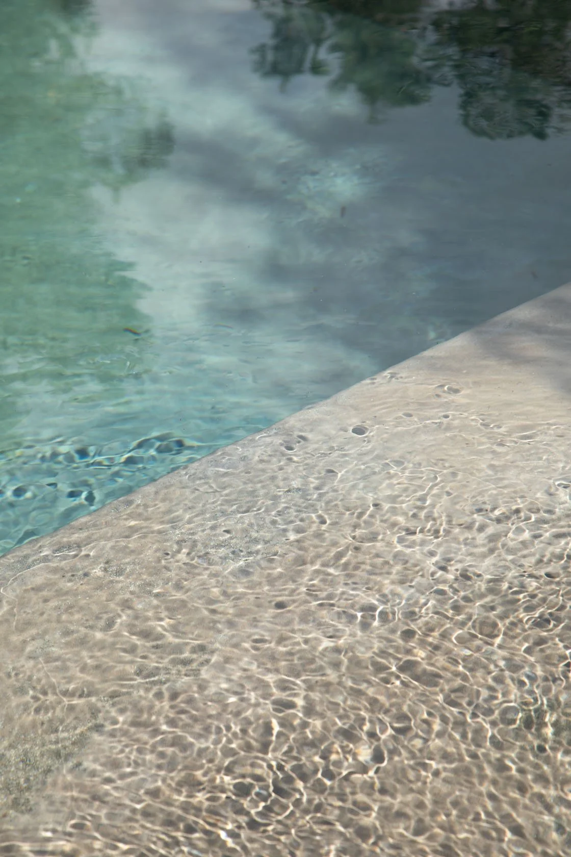 Close-up of a swimming pool's edge with clear water, showing reflections and ripples on the water's surface.