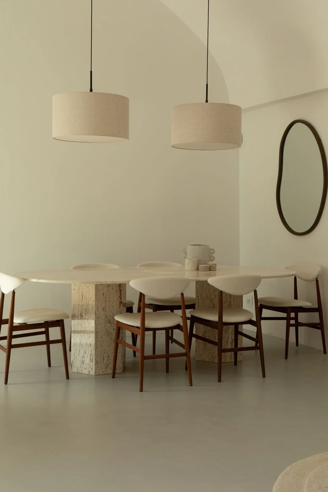 Dining room with round wooden table and six white chairs, modern light fixtures, and a round mirror on the wall.
