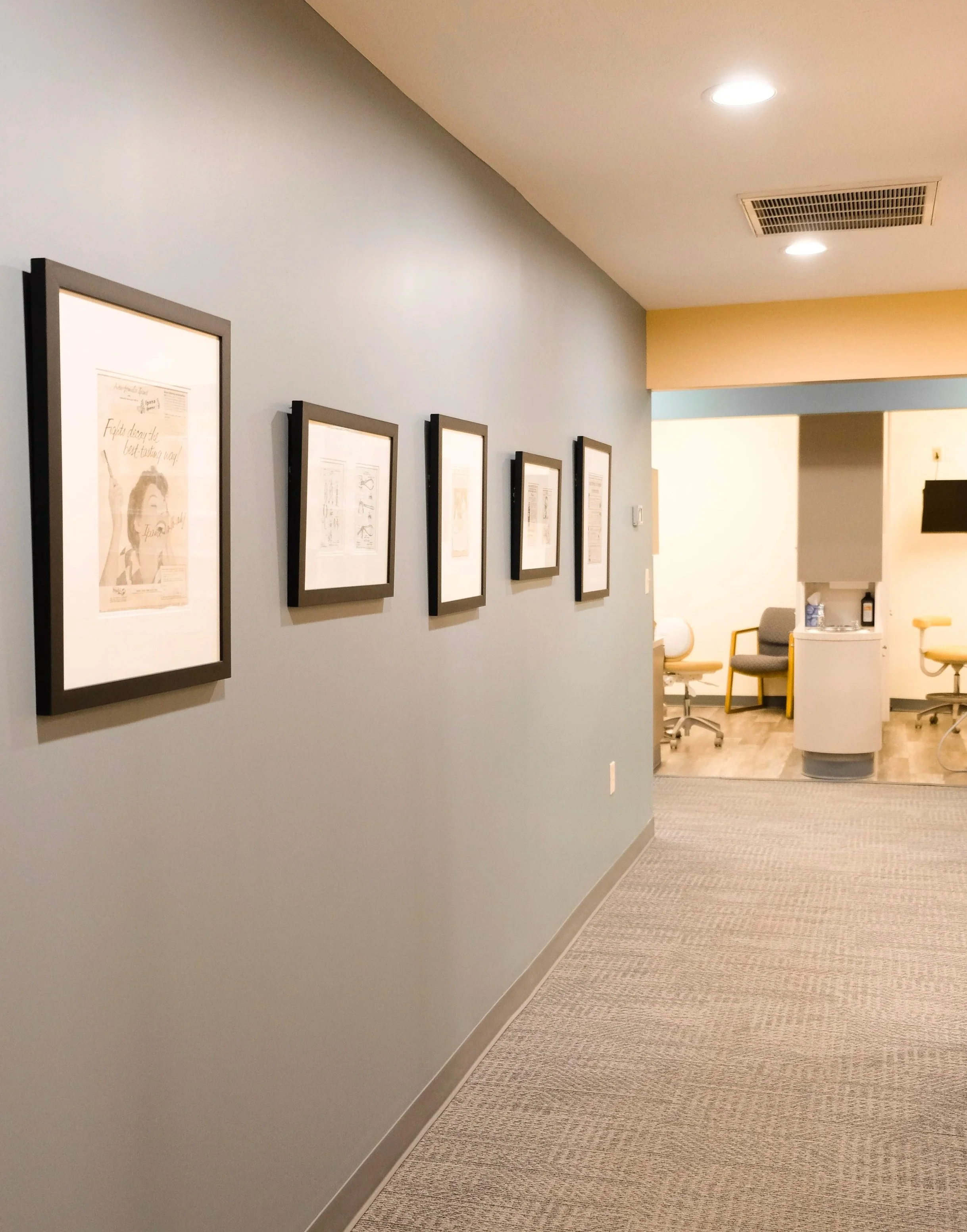 Hallway with framed pictures on a light blue wall leading to a small waiting area with chairs and a water dispenser.