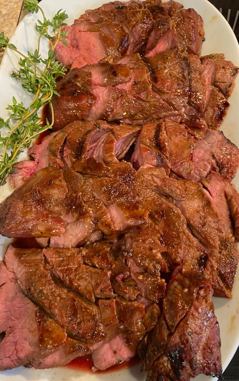 Sliced cooked beef roast garnished with sprigs of fresh thyme on a white platter.
