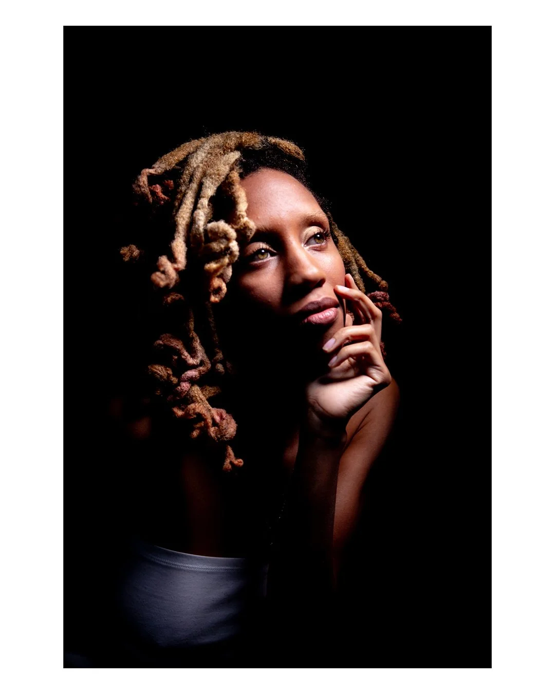 Portrait of a woman with long blonde dreadlocks looking thoughtful against a black background