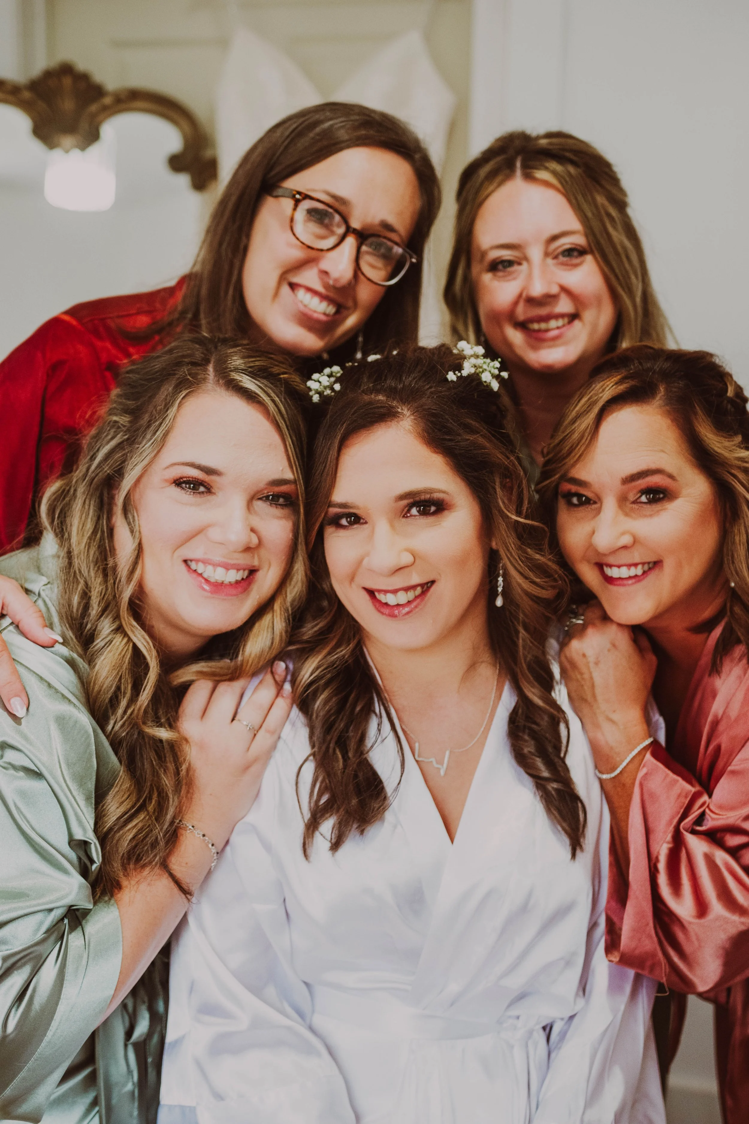A bride with four women surrounding her, smiling and close together, inside a room with elegant decor.