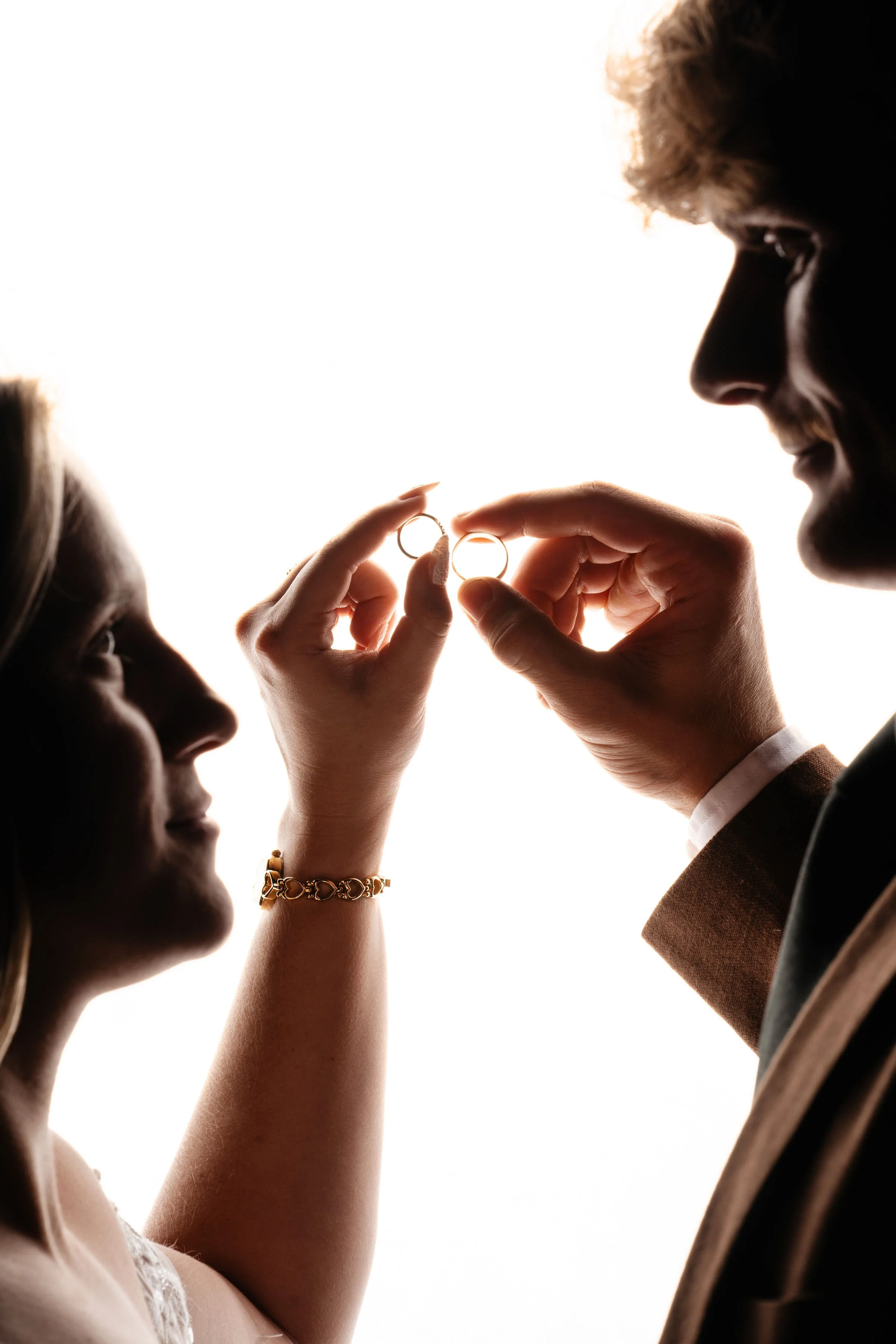 A couple exchanging wedding rings, with the bride and groom silhouetted against a bright background.