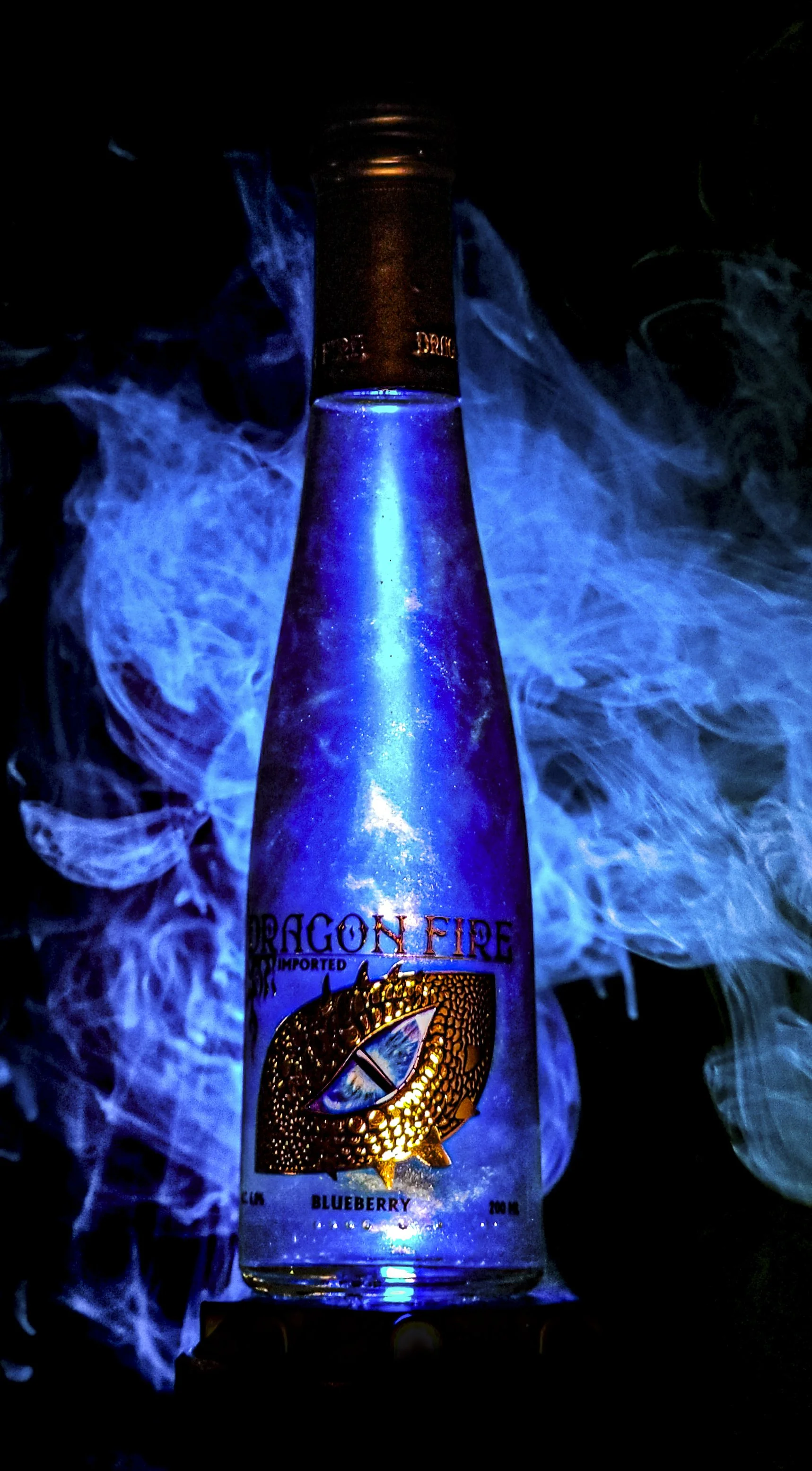 A bottle of Dragon Fire imported blueberry flavored beverage with blue smoke and lighting effects.