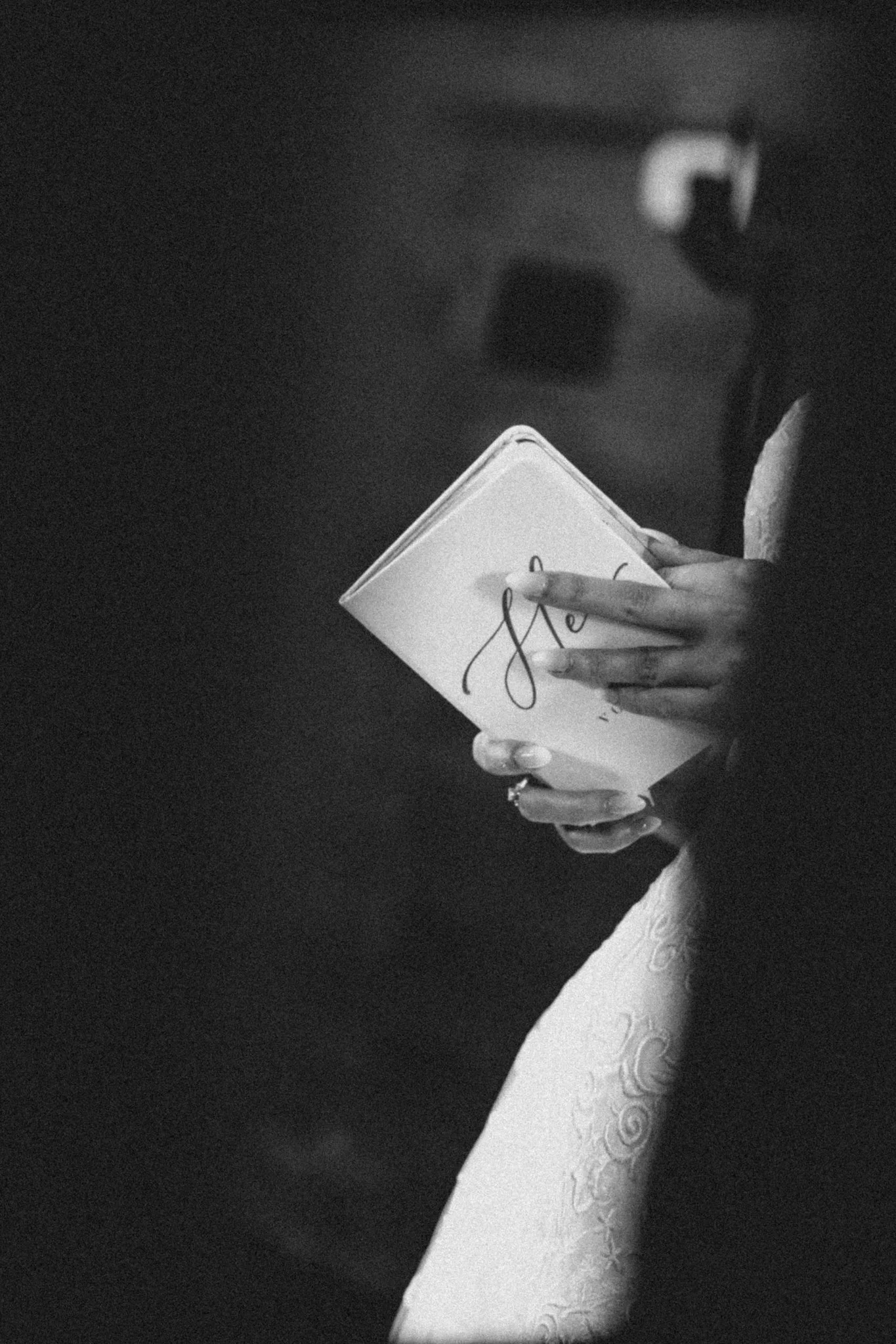 A person holding a notebook or journal with their right hand, with a lace sleeve visible, in a black-and-white photo.