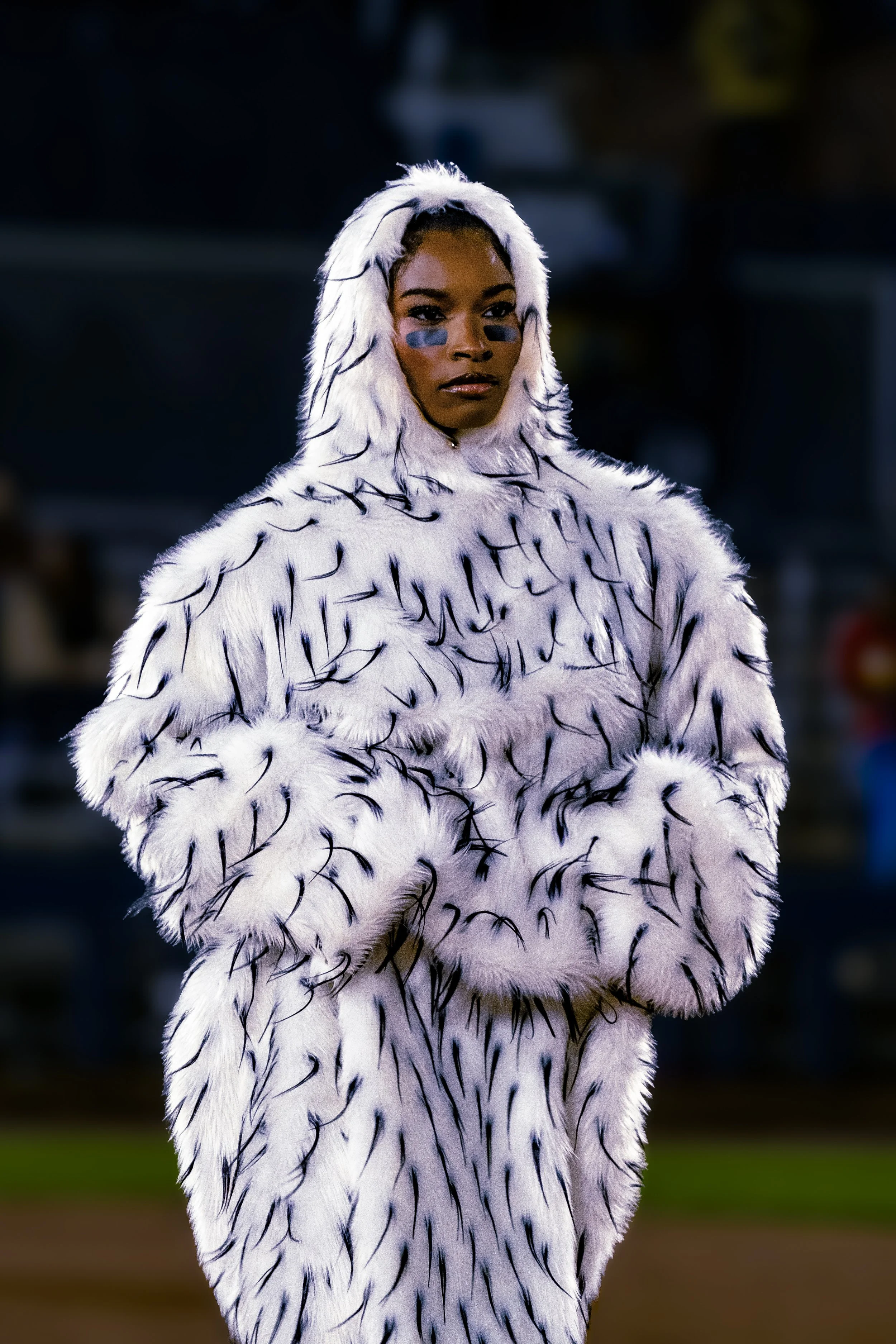 A woman wearing a white fur costume with black streaks, resembling a tiger or animal print, at night with a blurred background.