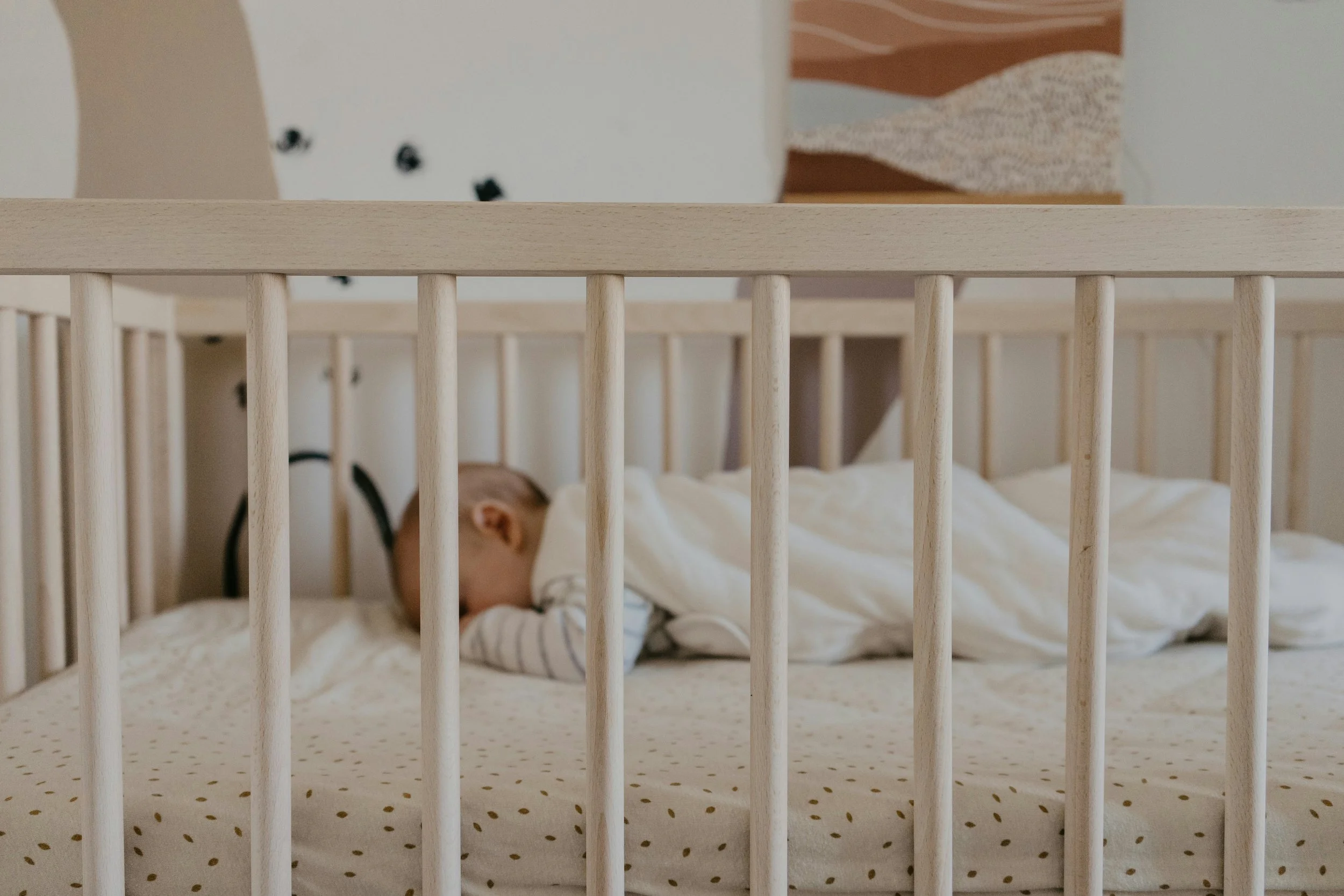 A baby sleeping in a crib with wooden bars.
