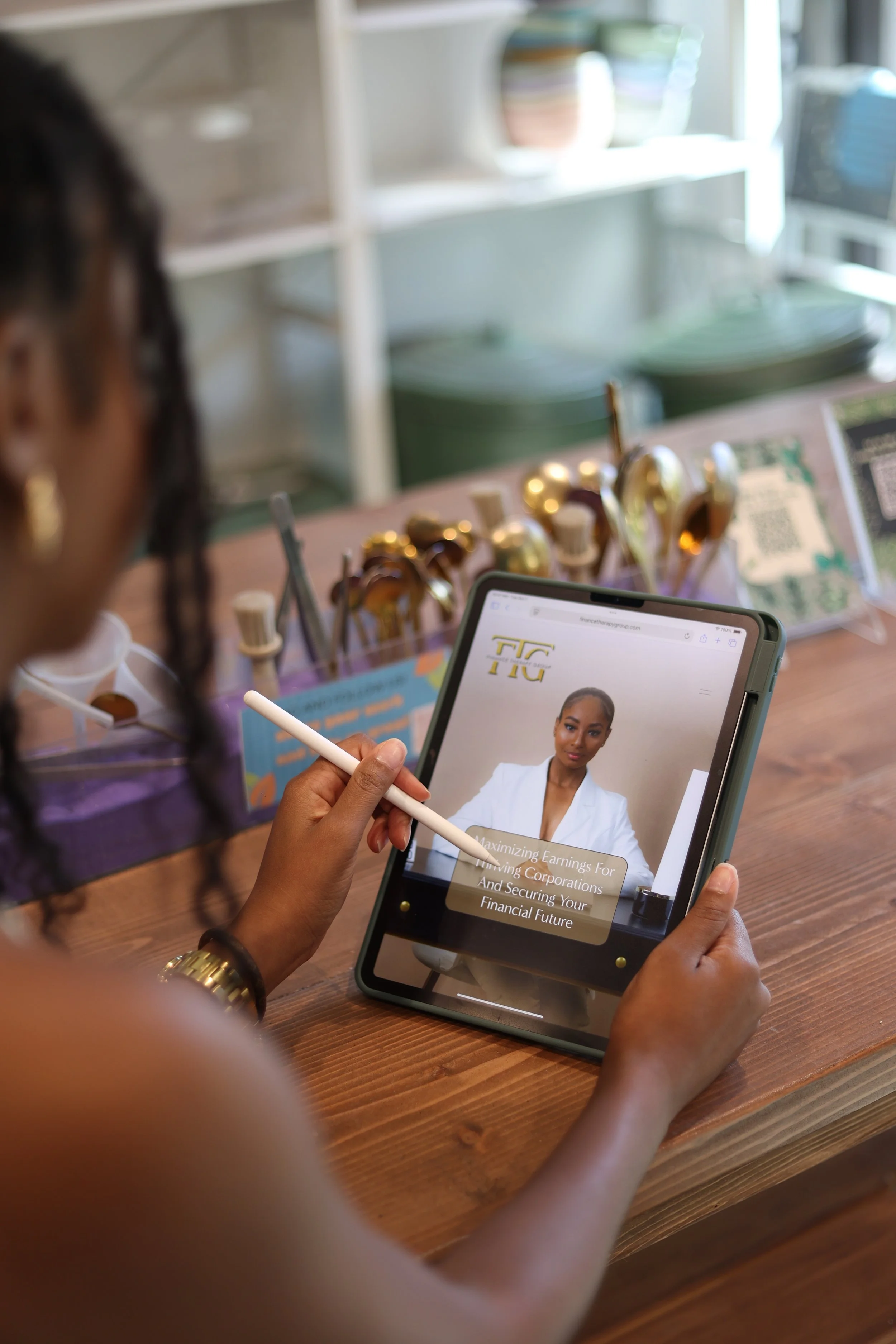 A woman using a stylus to browse a website on a tablet, featuring a woman in a white blazer and text about maximizing earnings for investing corporations and securing your financial future, in a store with jewelry or makeup brushes in the background.