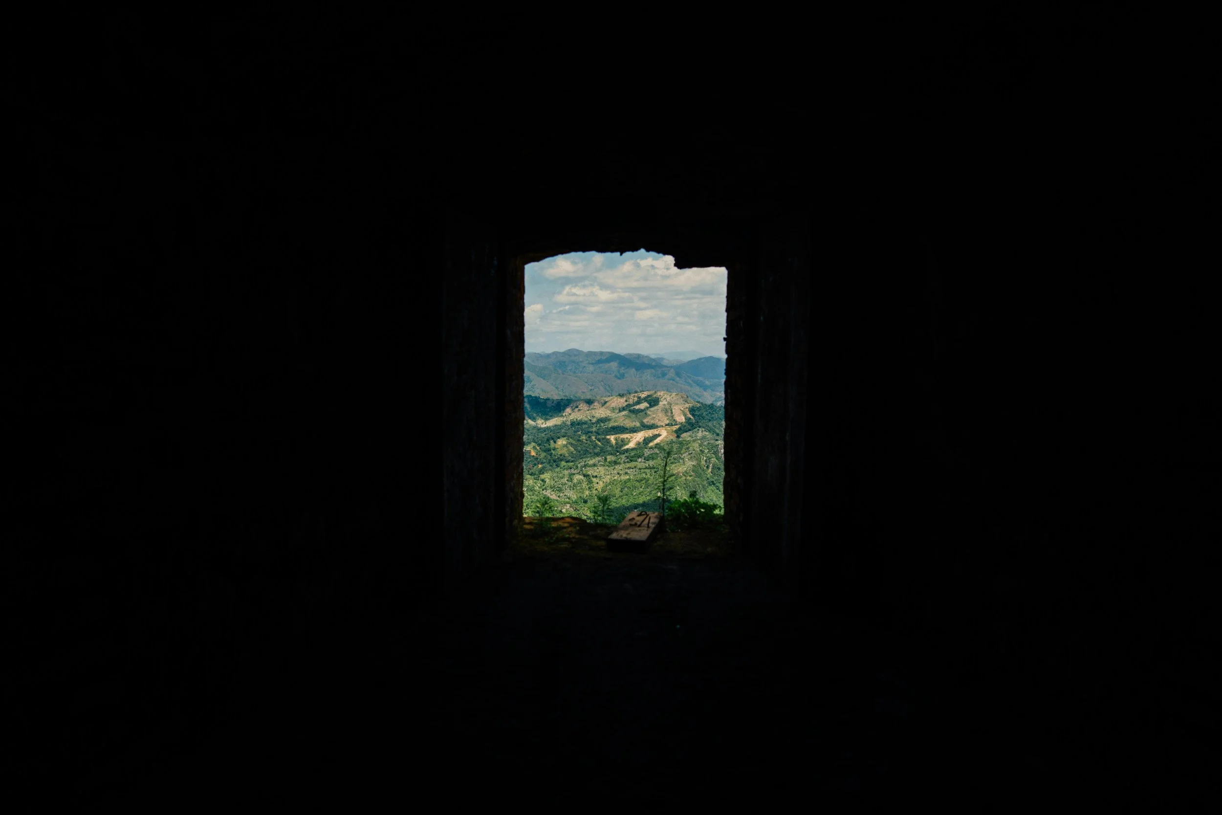 a window looking over a valley with green hills, surrounded by a dark black background