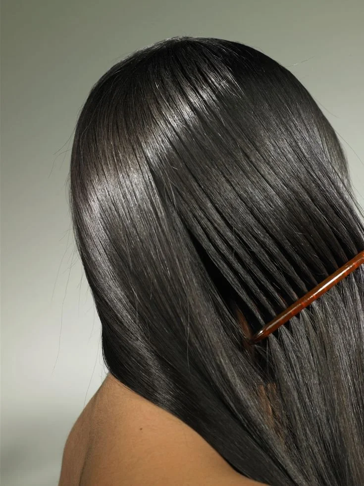 Close-up of a woman with long, straight, shiny black hair, holding a brown hairbrush.