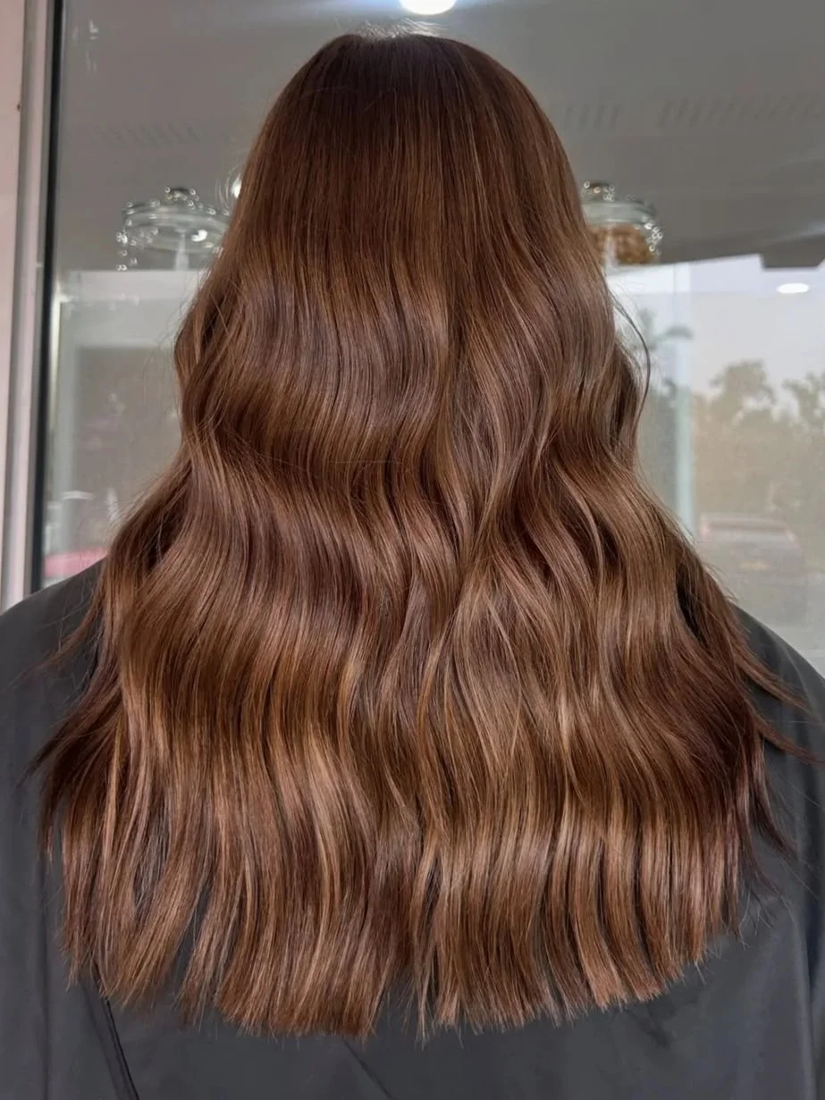 Back of a person's head with long, wavy, reddish-brown hair.