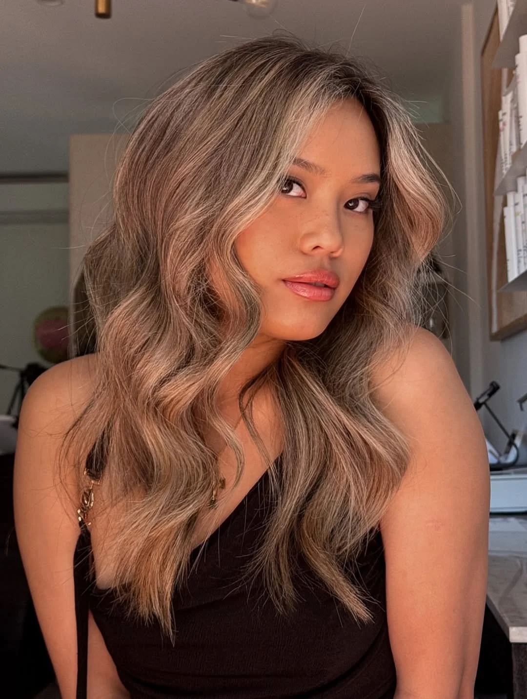 A young woman with long, wavy, blonde hair taking a selfie indoors, with a neutral expression on her face.