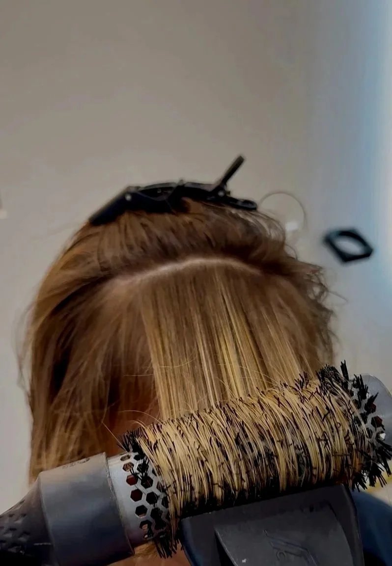 A person getting their hair blow-dried with a round brush and hair dryer.