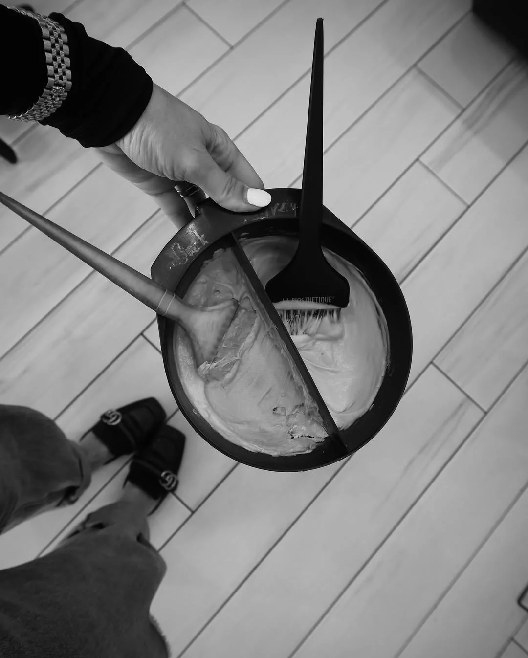 A hand holding a divided plastic container with ice cream, two spoons, and a small brush on top of a wooden floor.