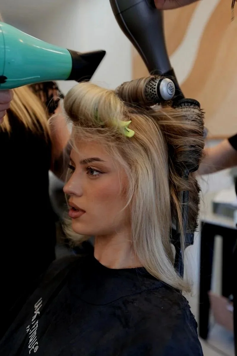 A woman with blonde hair getting her hair styled with rollers in a salon.