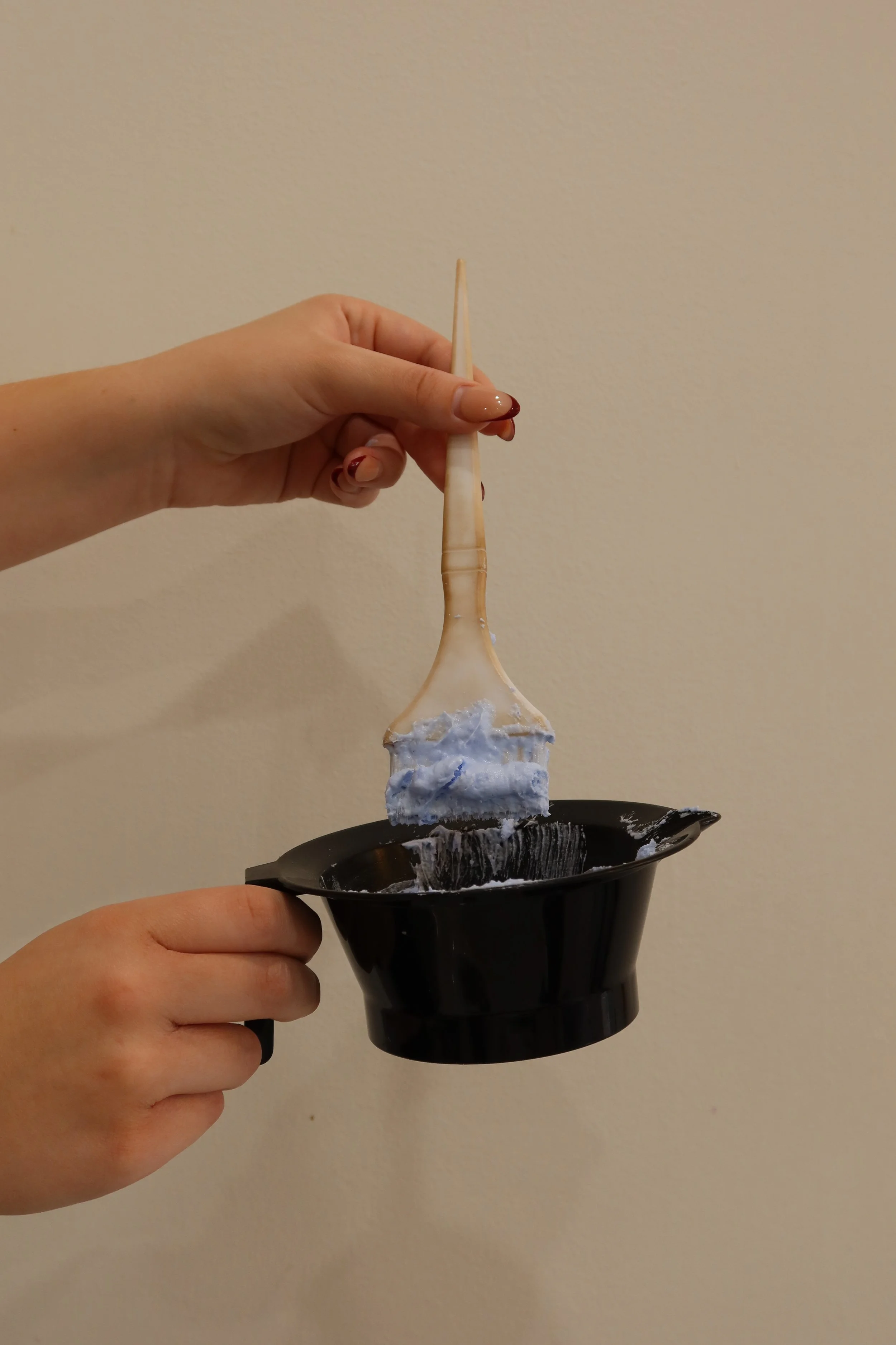 Person holding a small black bowl with white and blue fabric inside, using a beige spatula to scrape blue and white substance.