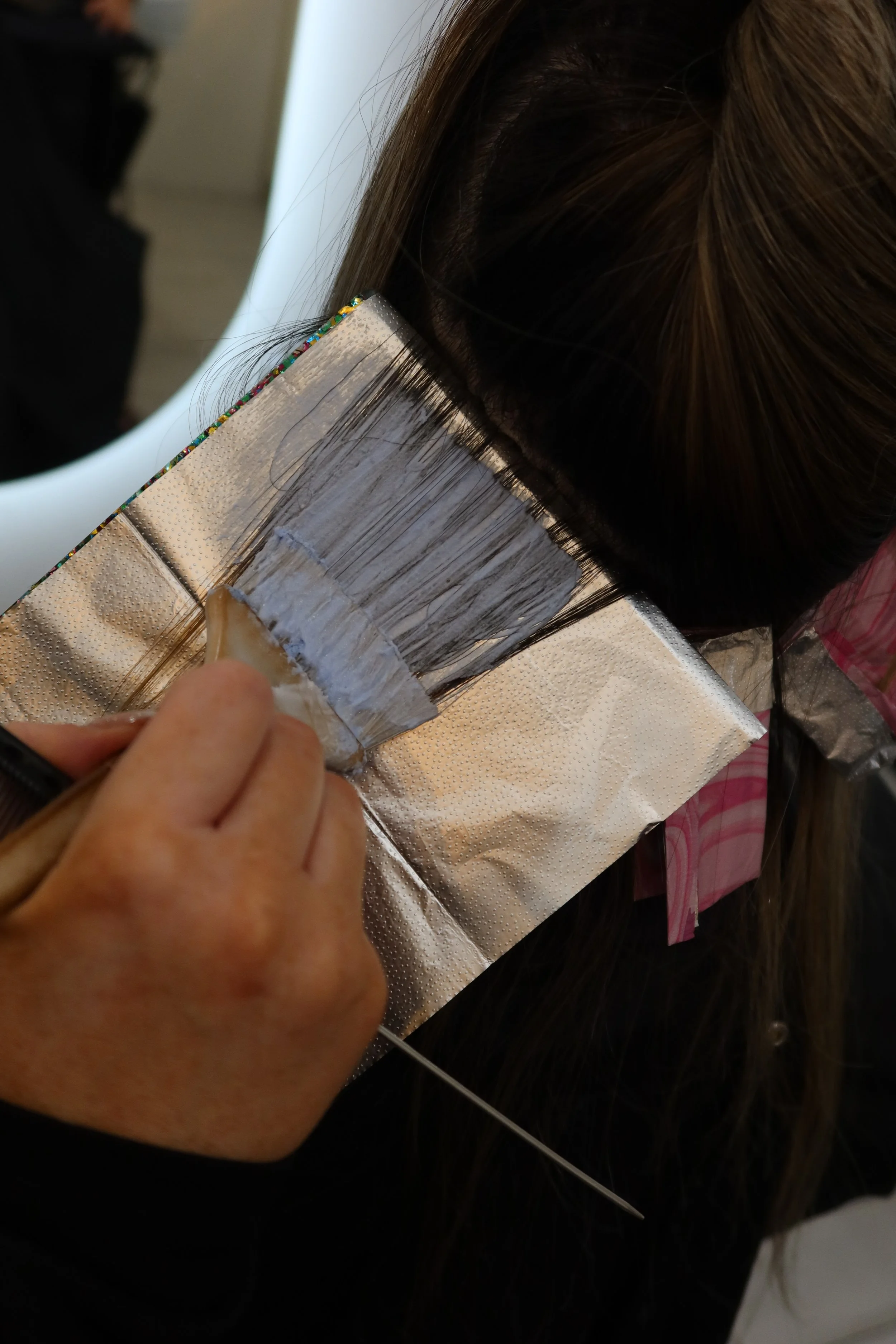 A person applying hair dye to long brown hair at a salon, with a foil cap and brush.